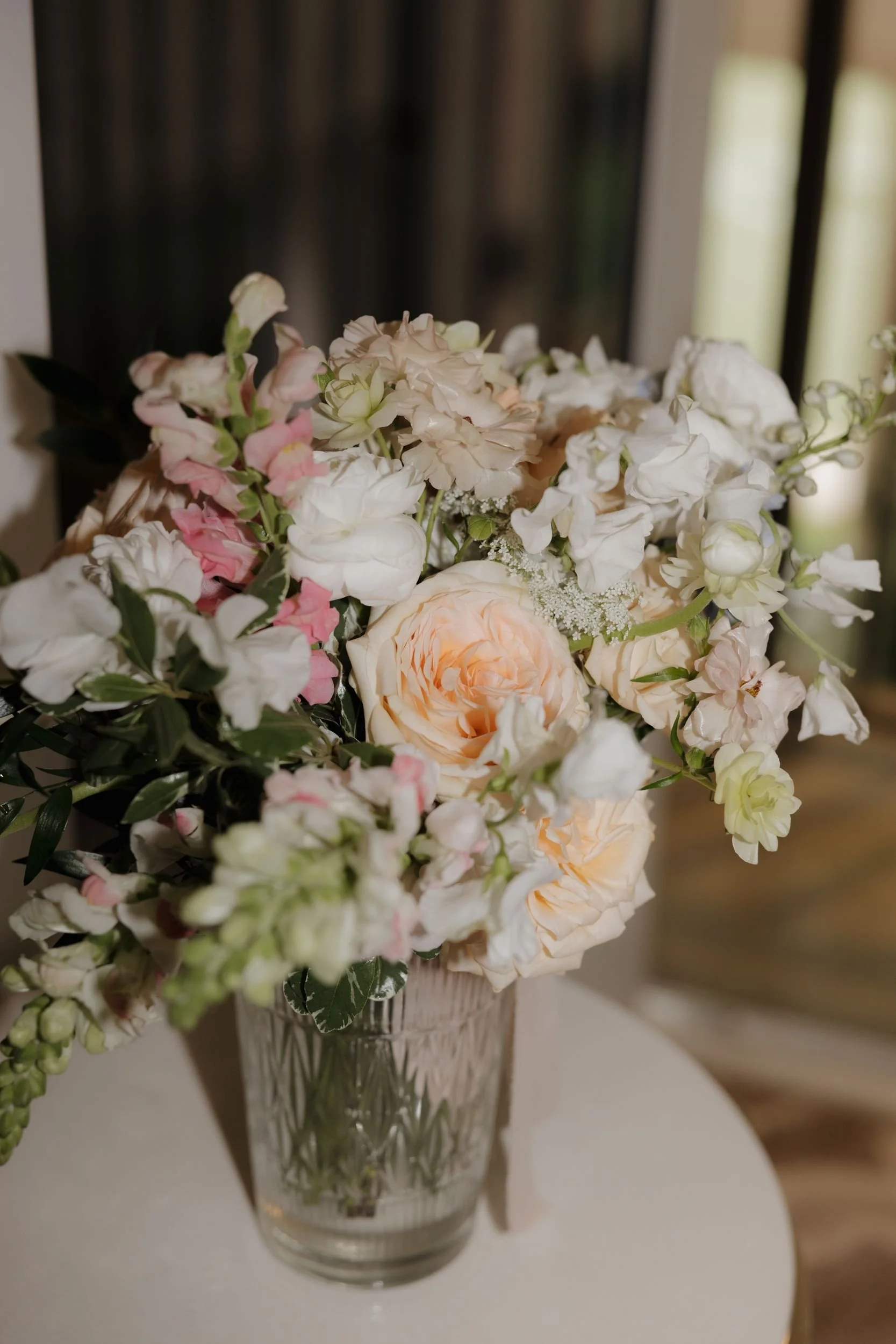 Floral centerpiece of peach garden roses, white snapdragons, and blush blooms in a mercury glass vase