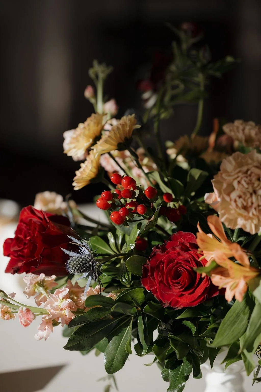 Tall arrangement of burgundy roses and white blooms in a footed vase