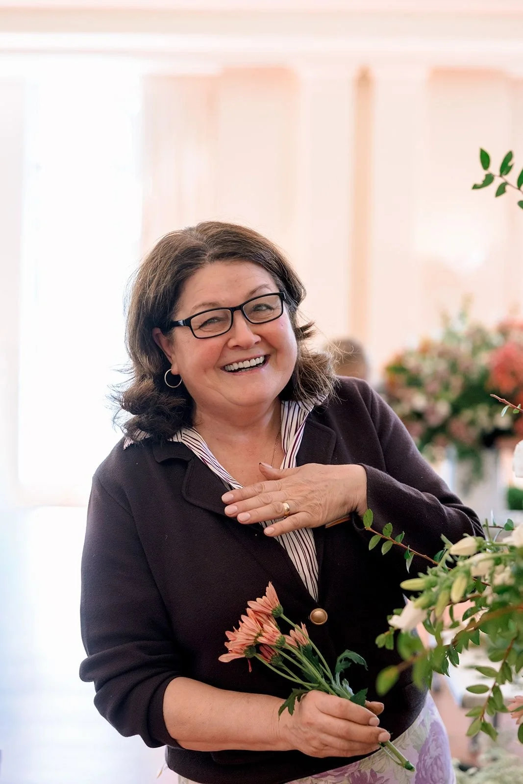 Lead floral designer standing confidently in front of a colorful ceremony floral arch of purple, pink, and blue flowers at an outdoor wedding venue.