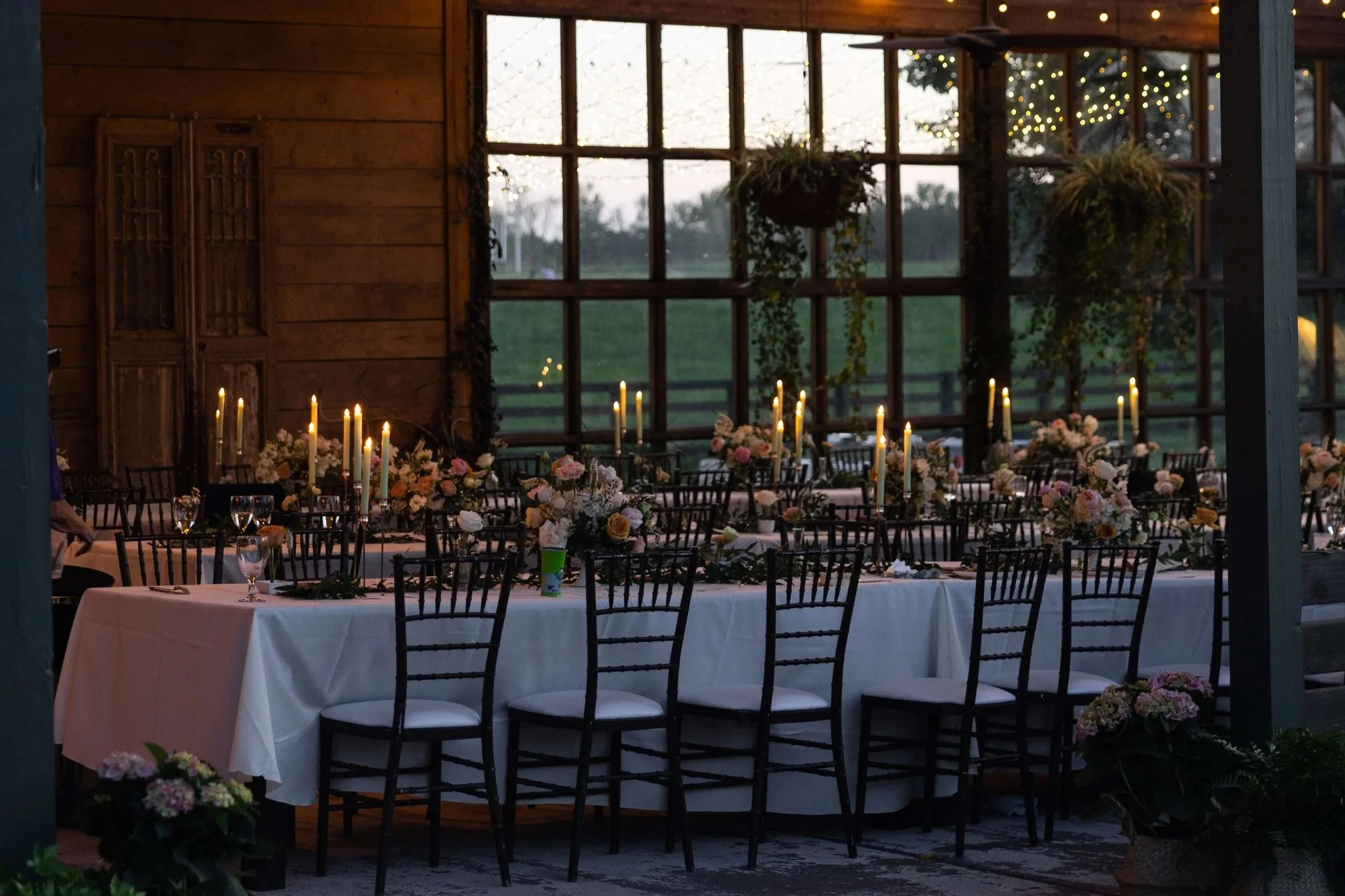 Romantic candlelit wedding reception inside rustic barn pavilion with wooden frame doors, elegant floral centerpieces, chiavari chairs, and taper candles at Wild Daisy Farm in Molena Georgia