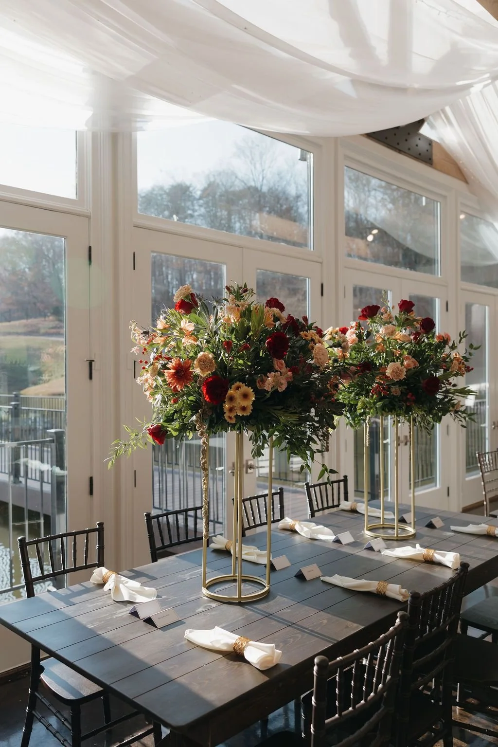 Long banquet table with tall elevated floral centerpieces, place settings, and draped windows
