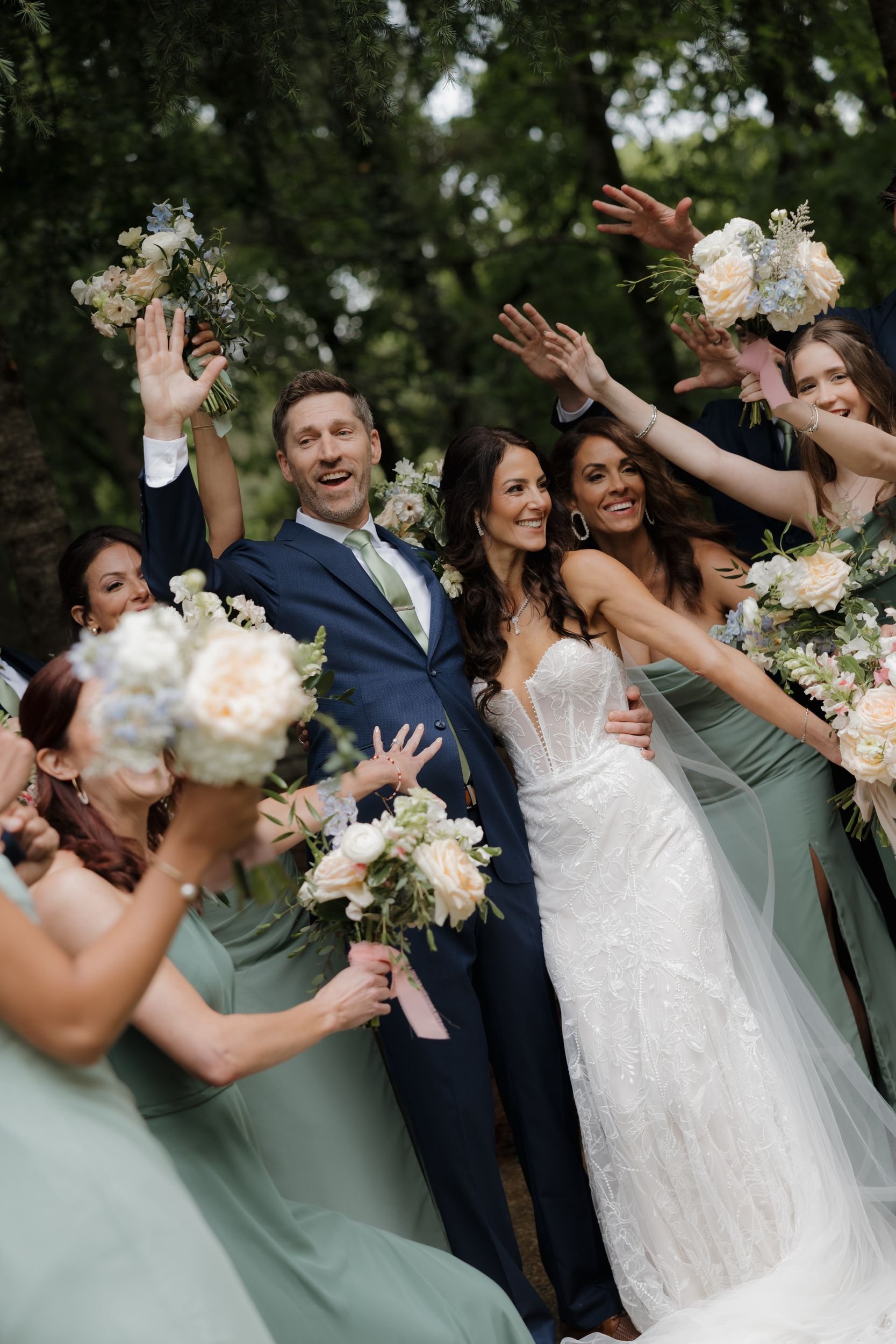 Bride and groom celebrating with their bridal party, who raise ivory and blush bouquets