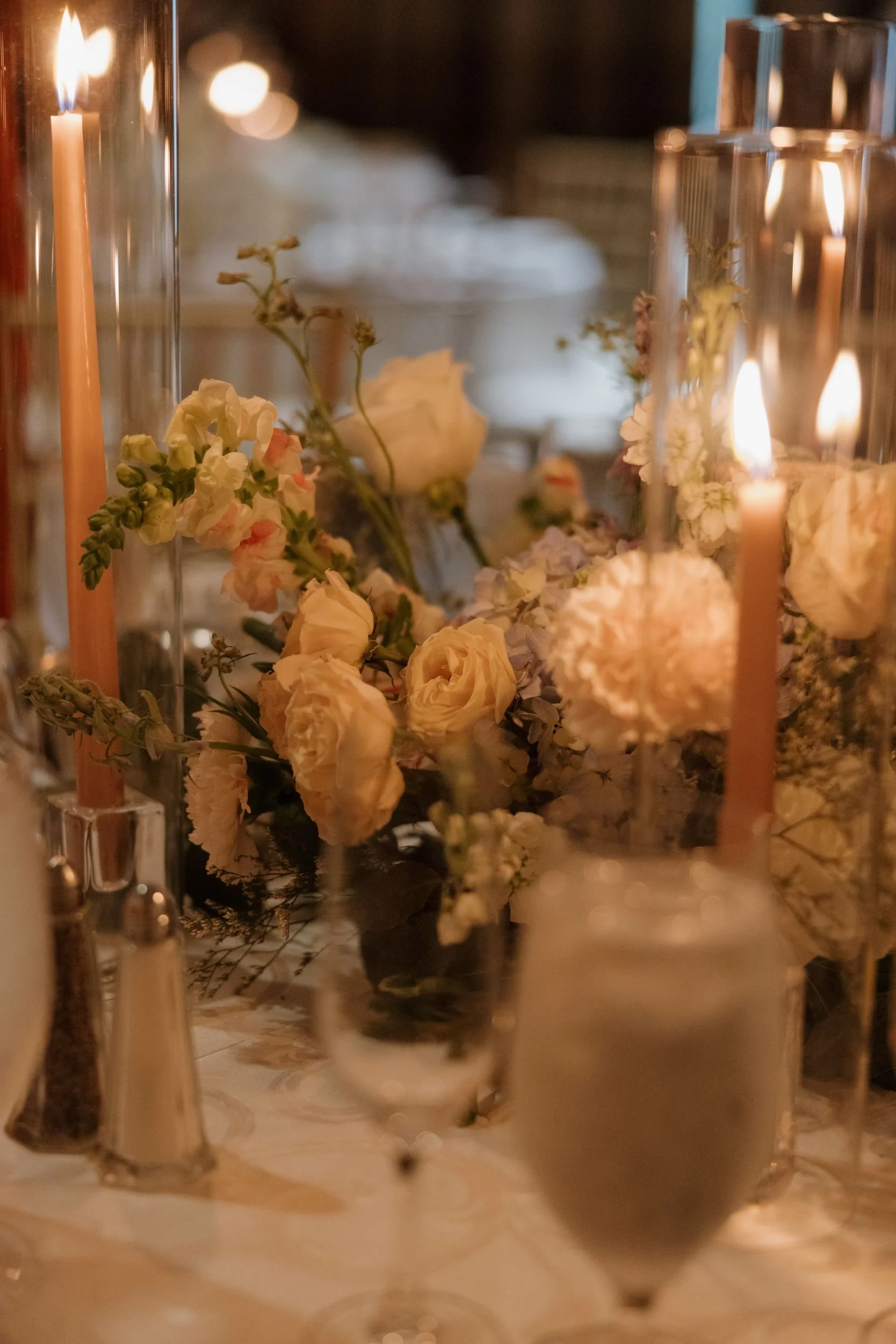 Candlelit centerpiece detail of peach and cream roses and a dahlia among tall tapers and glassware