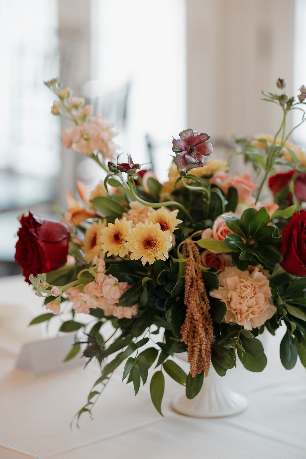 Lush centerpiece of terracotta, peach, and burgundy blooms on a reception table