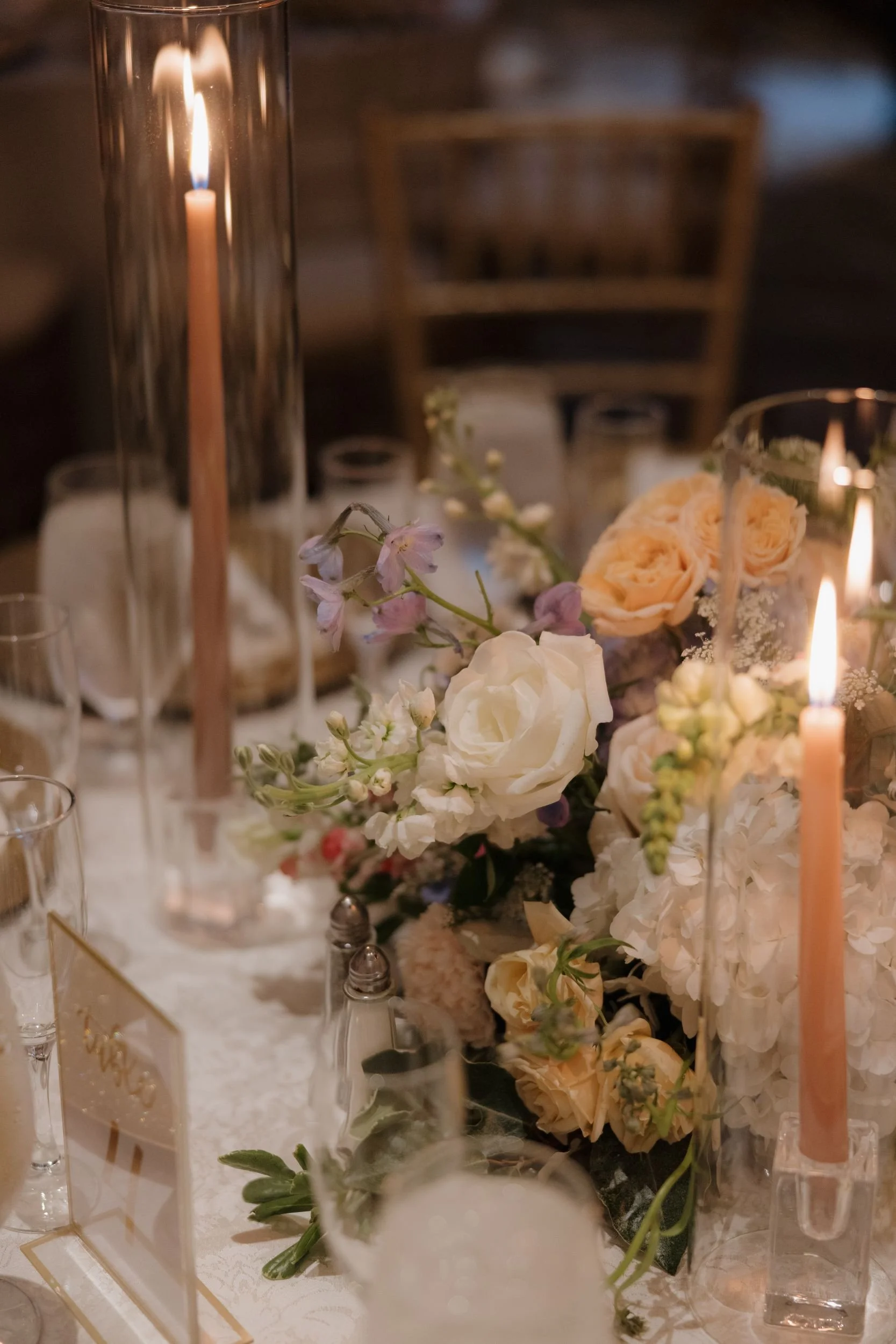 Reception table detail with a centerpiece of peach roses, white, and lavender blooms among tall taper candles