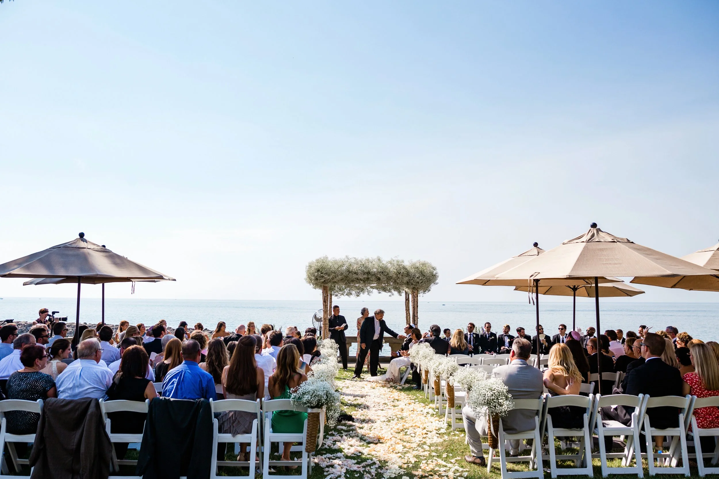 Market umbrellas shading rows of ceremony chairs at an outdoor summer wedding