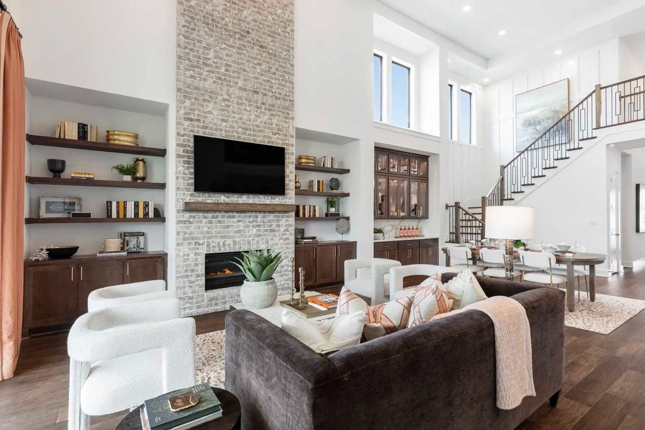 Empty living room with a stone fireplace, a ceiling fan, and a large window, with protective paper on the floor.