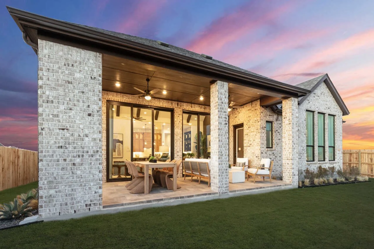 Modern brick house with covered patio, outdoor furniture, and a wooden fence, during sunset.