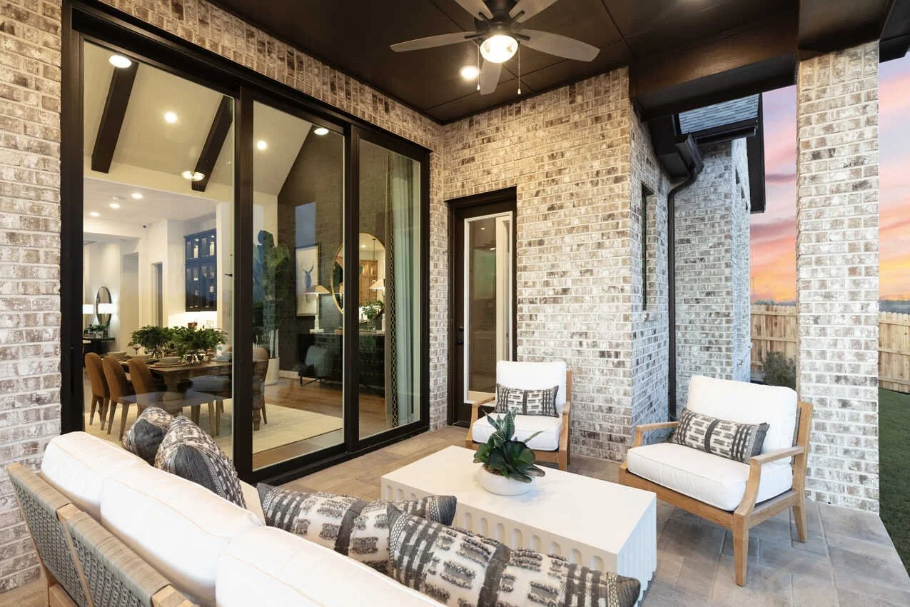 Covered outdoor patio with white sofa, two armchairs, and a coffee table, overlooking a backyard at sunset.