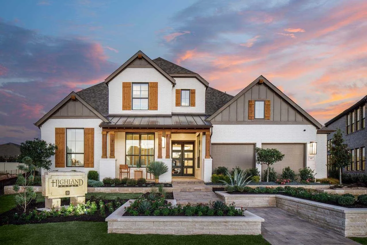 A modern two-story house with a landscaped front yard at sunset, featuring white walls, wooden accents, and a double garage.