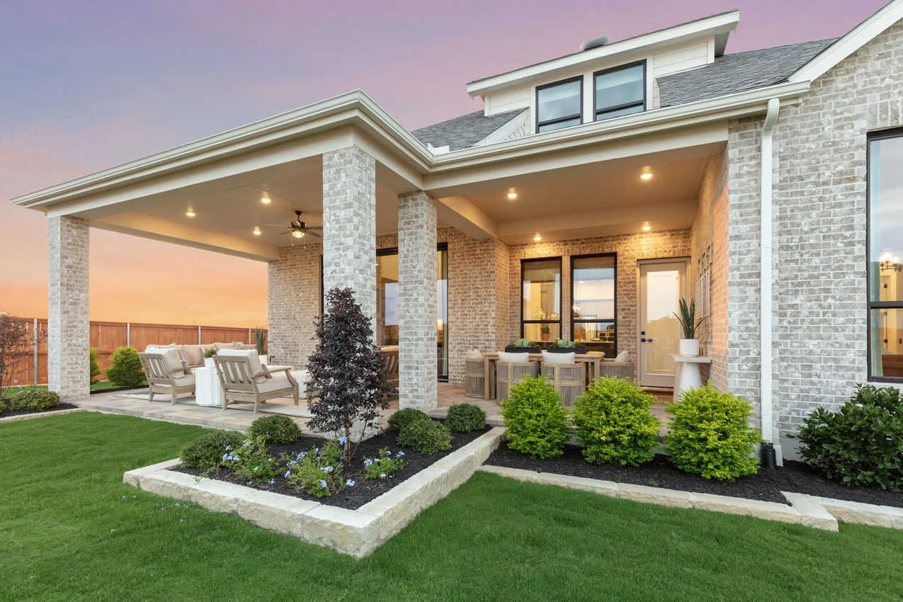 Beautiful backyard patio with outdoor seating, dining area, lush landscaping, and sunset sky.