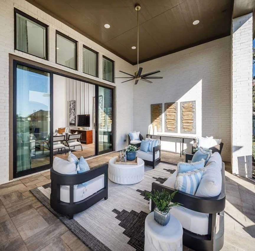Outdoor patio with white brick walls, black and white furniture, a ceiling fan, and an area rug. The patio is partially open with sunlight streaming in.
