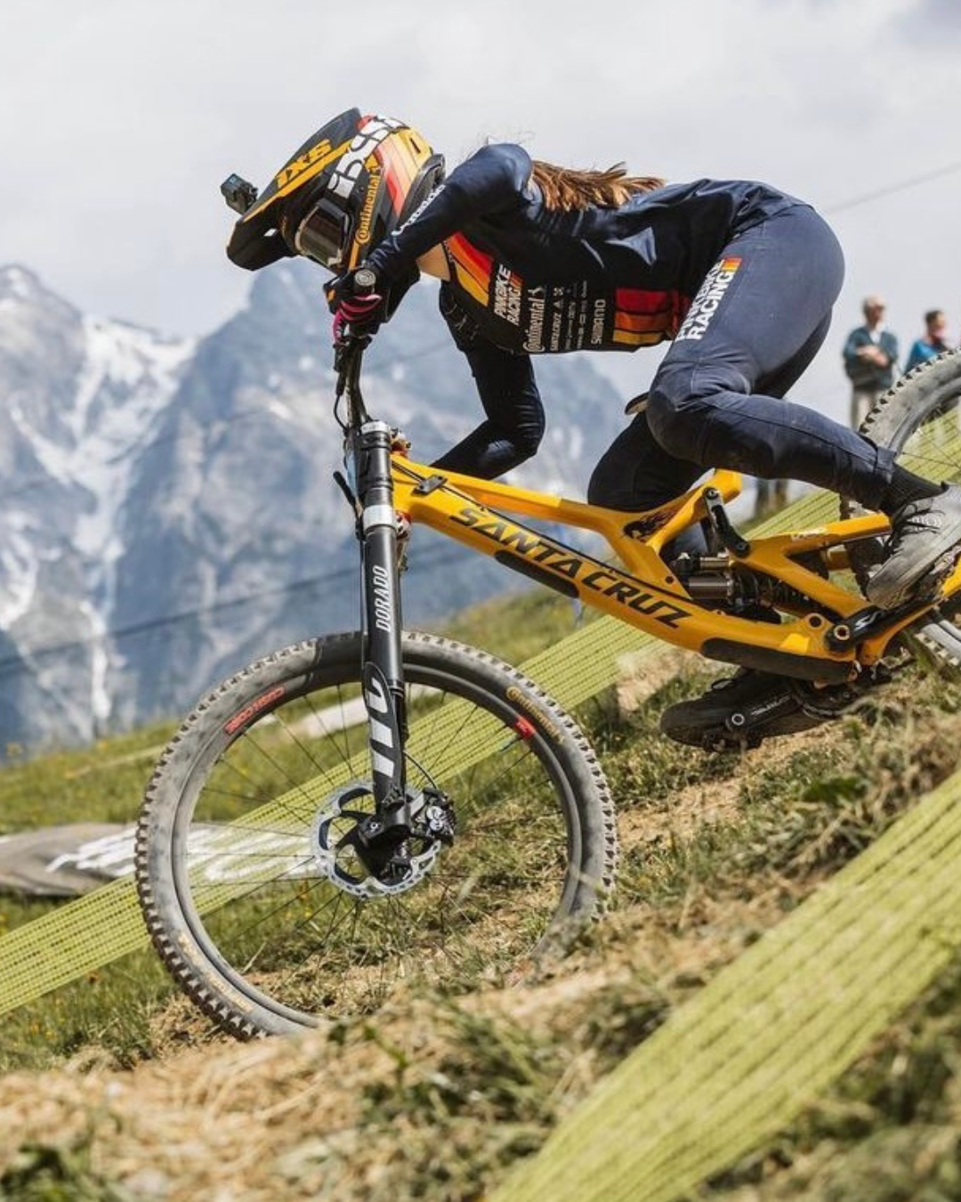 Mountain biker racing downhill on a yellow Santa Cruz bike with mountains in the background.