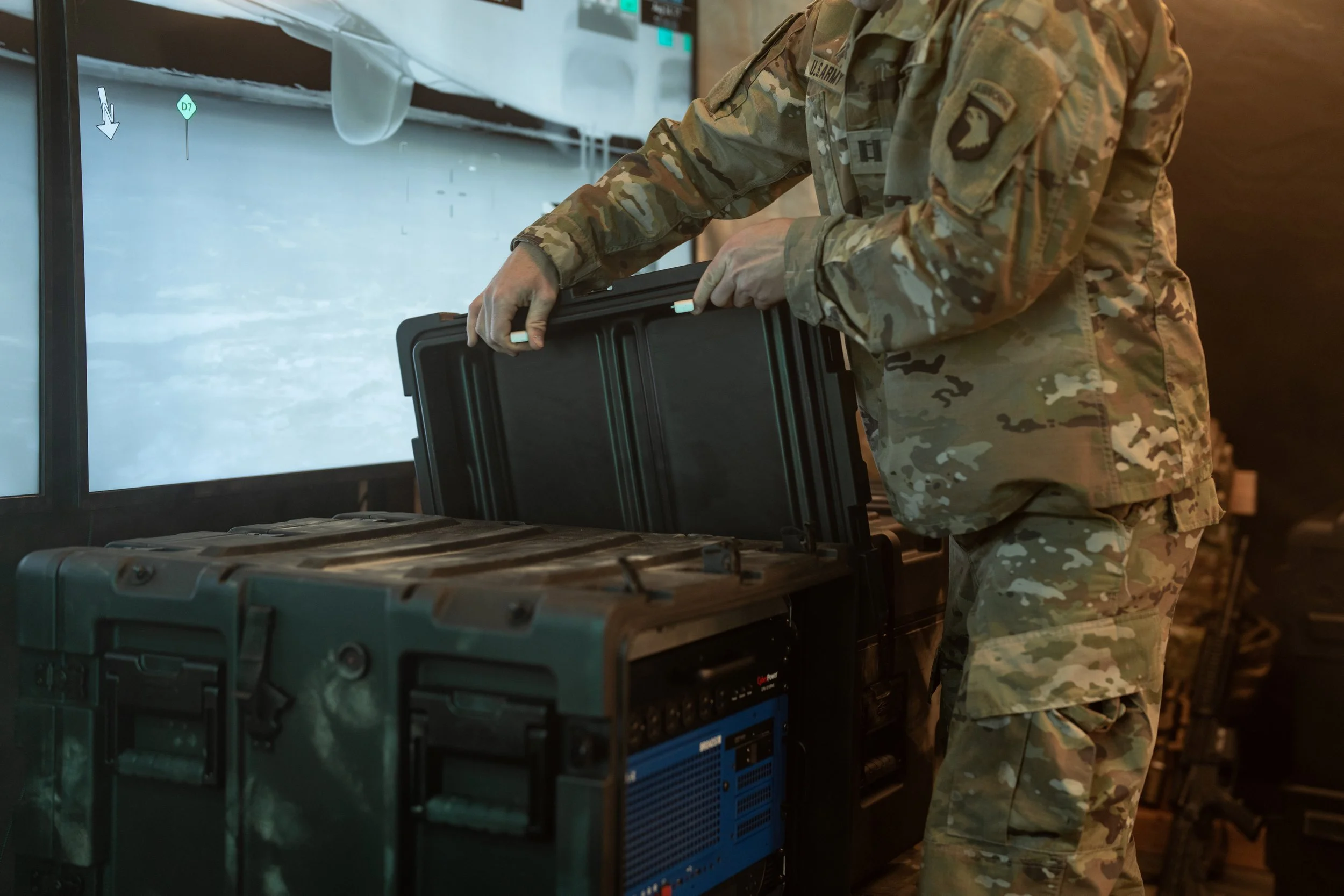 A person in U.S. military camouflage uniform handling equipment or supplies, possibly at a military facility or during a deployment, with a focus on his torso and hands.