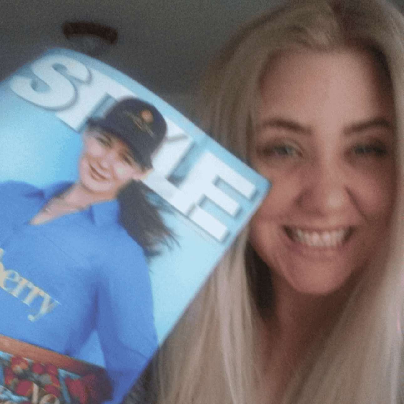 A smiling woman with long blonde hair holding a magazine with a person on the cover.