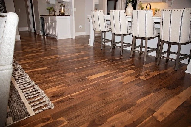 Modern kitchen with wooden flooring, high-back chairs, and a white countertop with decorative items.