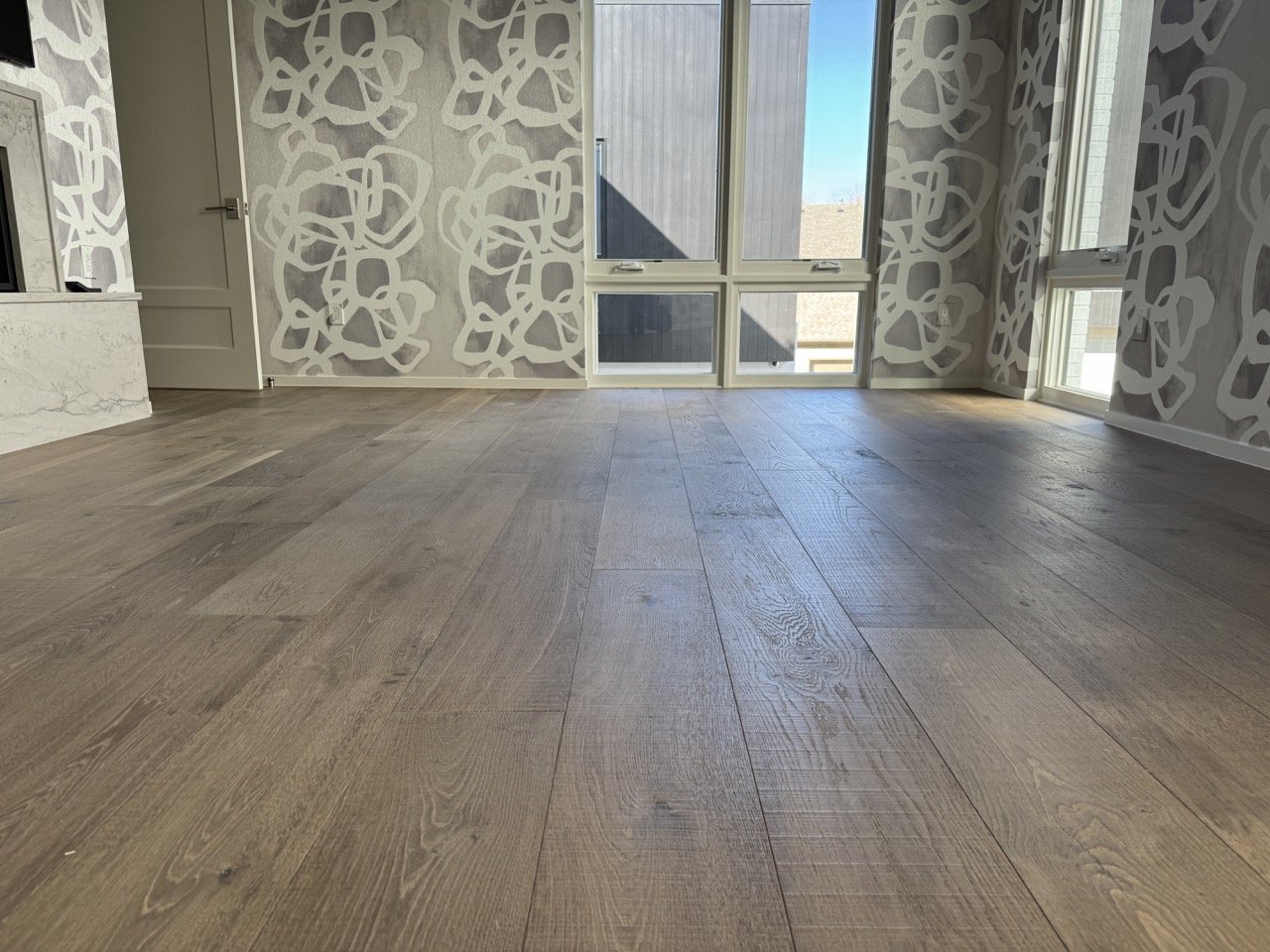 Spacious empty room with wood flooring, large windows, and abstract patterned wallpaper, featuring a marble surface to the side.