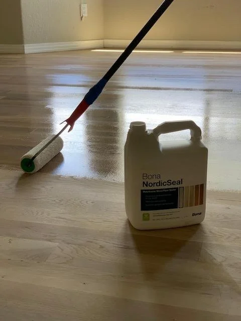 Floor being sealed with a roller and Bona NordicSeal container on a wooden floor.