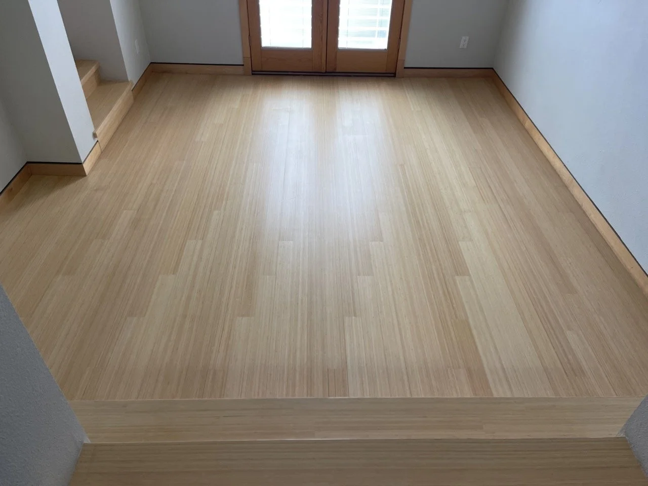 Empty room with light wood flooring and double doors with blinds.