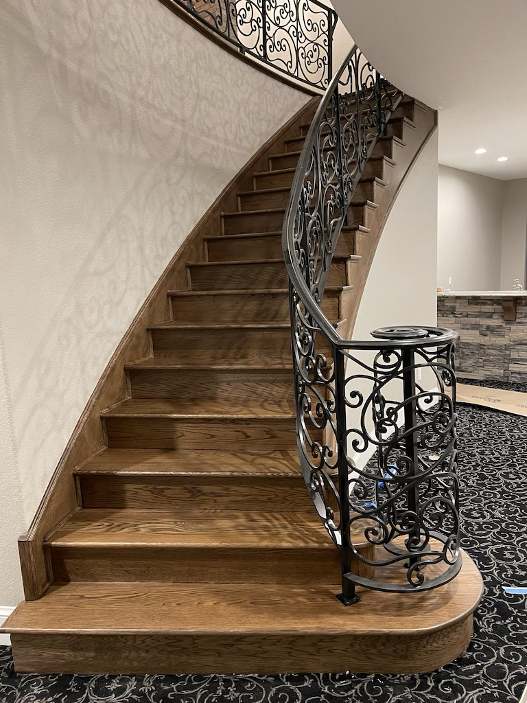 A curved wooden staircase with a decorative wrought iron railing in an indoor setting.
