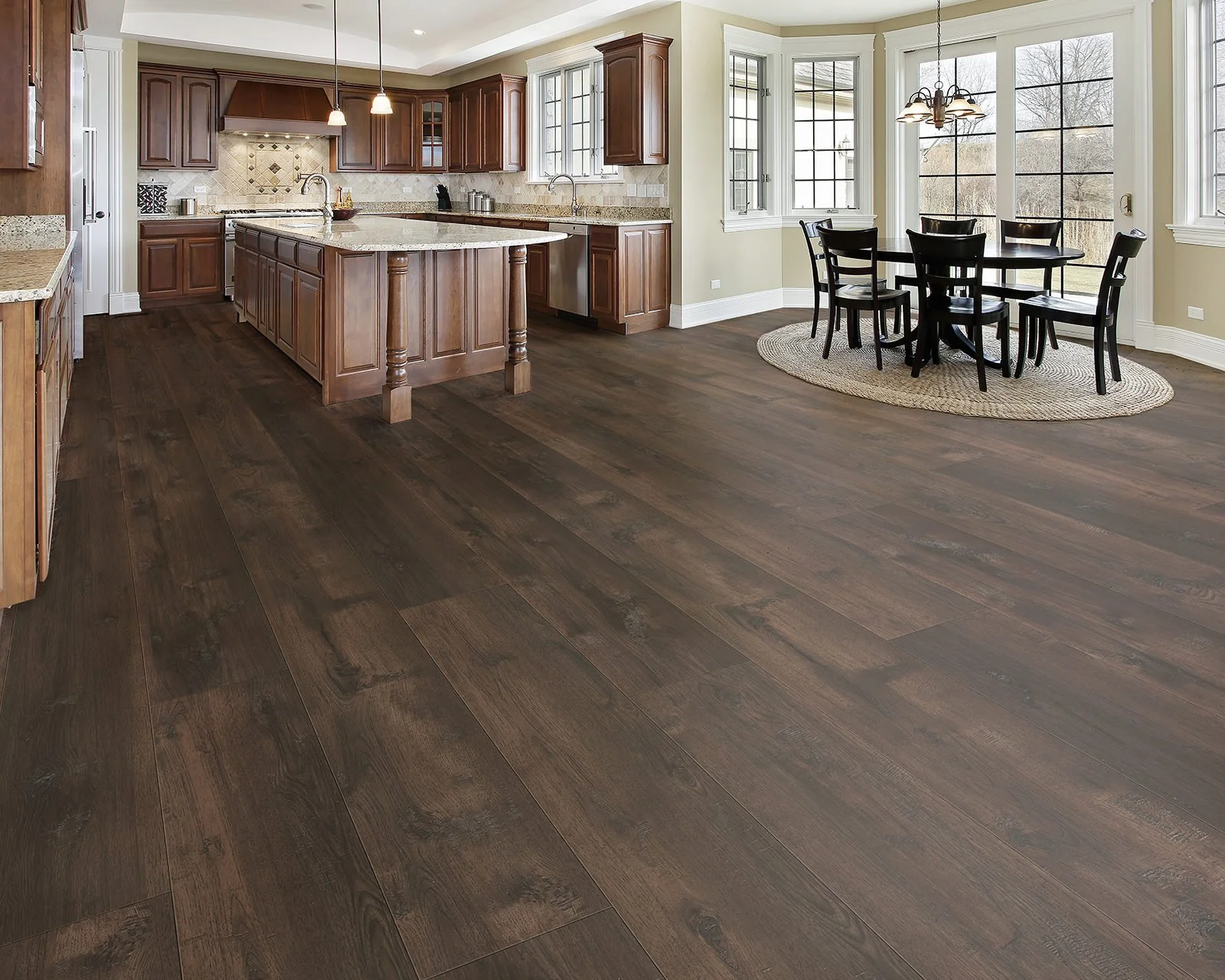 Open kitchen and dining area with dark wood flooring, wooden cabinets, and a round dining table with six black chairs near large windows.