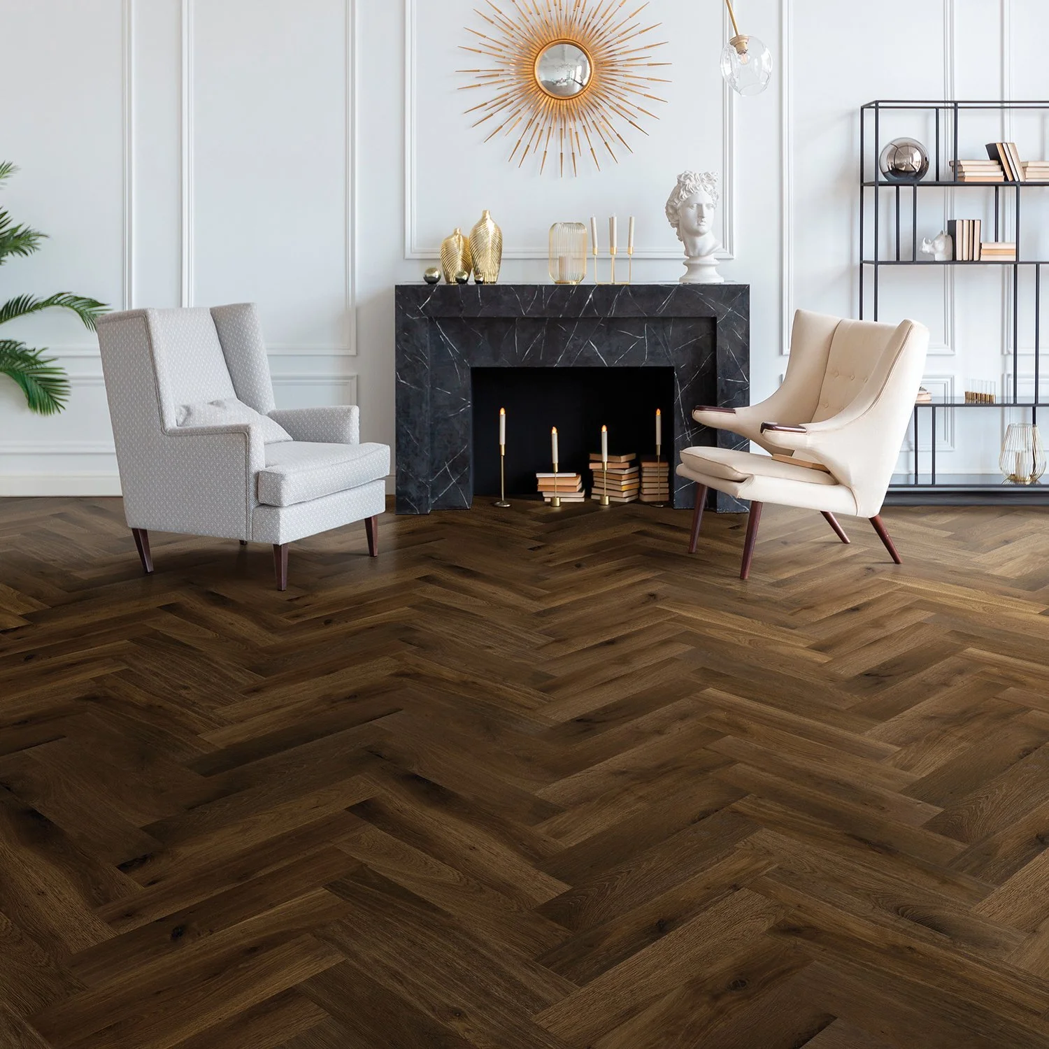 A modern living room with two armchairs, a black marble fireplace, gold and white decorative items, and wood flooring in a herringbone pattern.