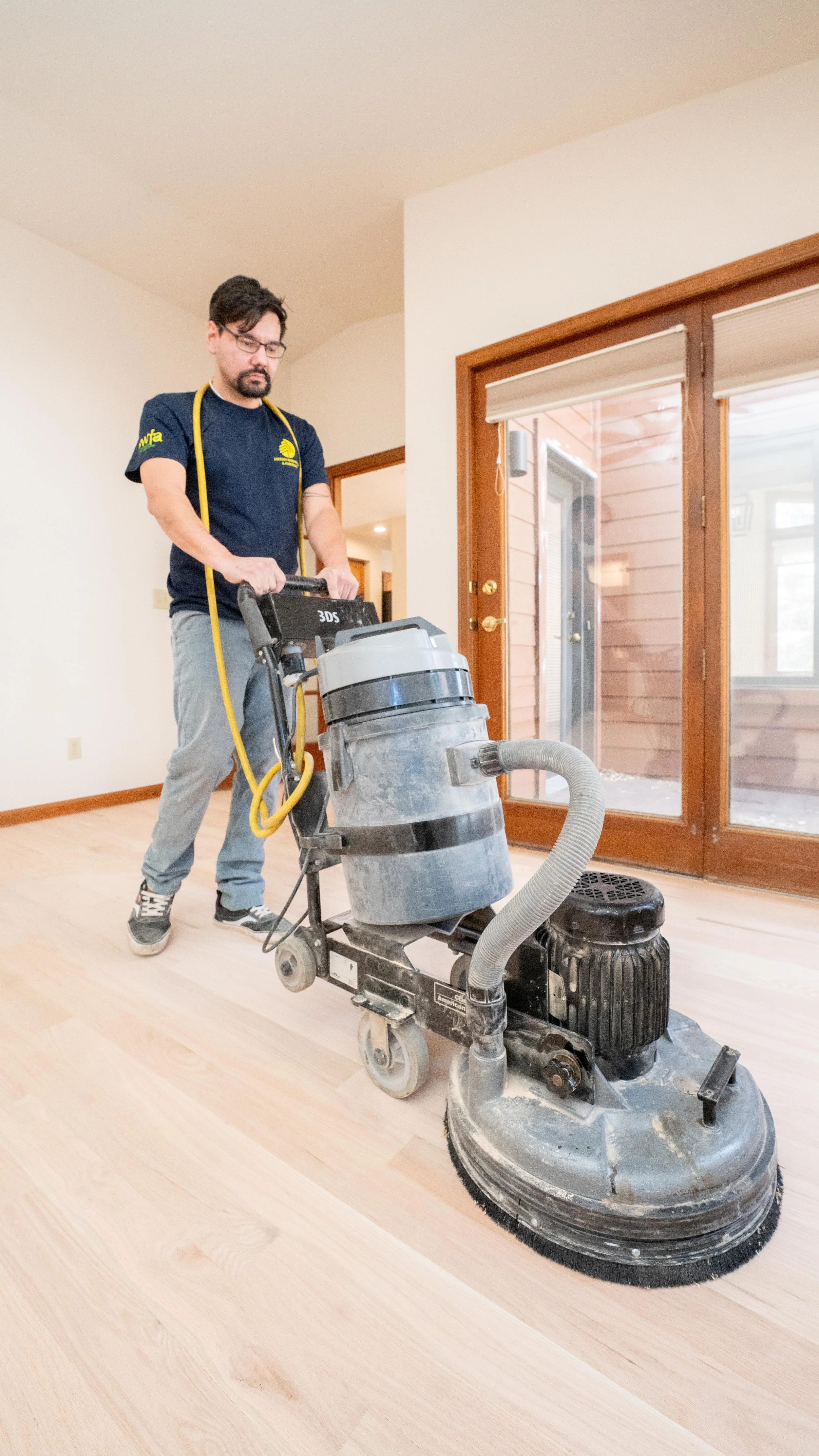 Person using a floor buffer on a hardwood floor in a room with wooden doors.