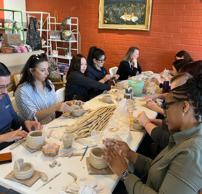 Group of people surrounding a table making ceramic art.