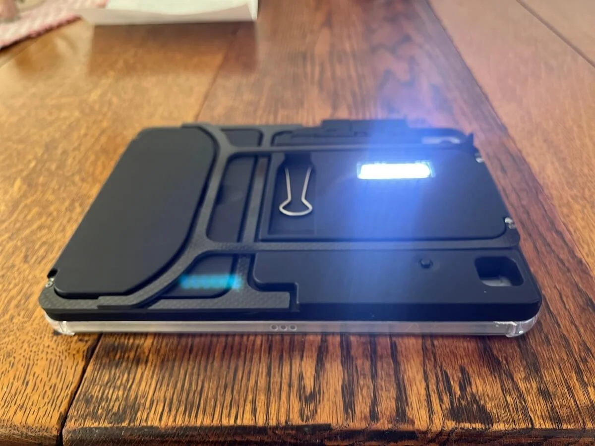 Bottom view of Case for Vision Solaris resting on a wooden table, showing the built-in illuminator turned on and glowing brightly beneath the device.