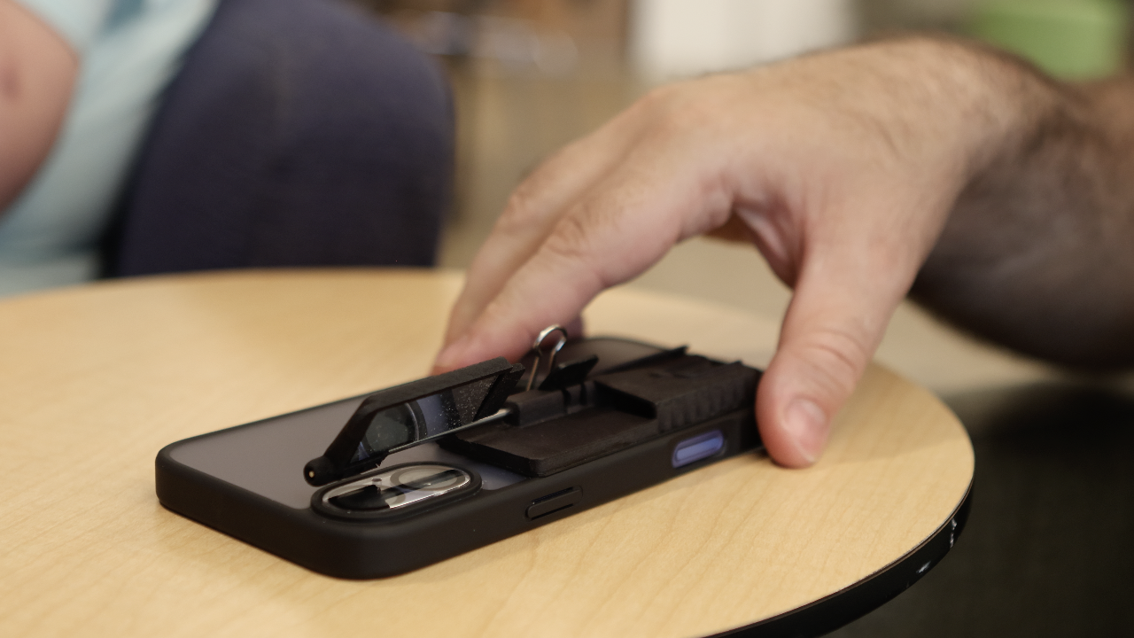 `An iPhone lies facedown on a table with a Case for Vision Ergo attached. The Ergo’s mirror is unfolded and upward at a 45-degree angle.