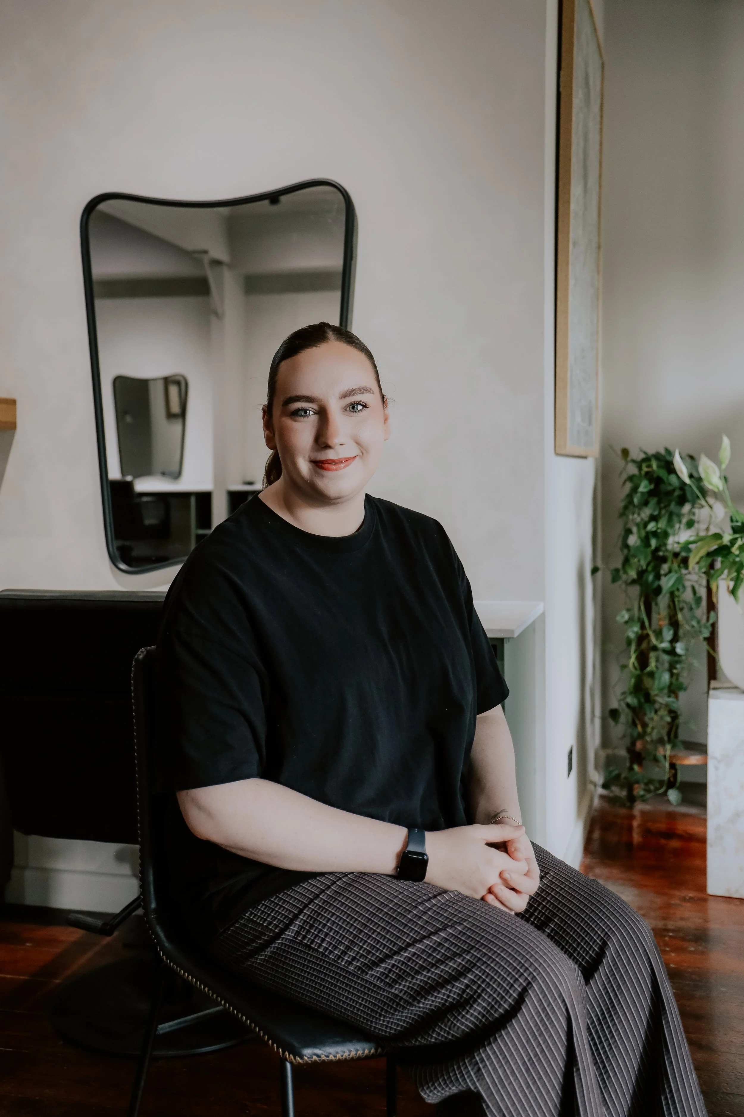 Hair stylist using a curling iron on a client's hair in a salon, with a black and white photo on the wall.