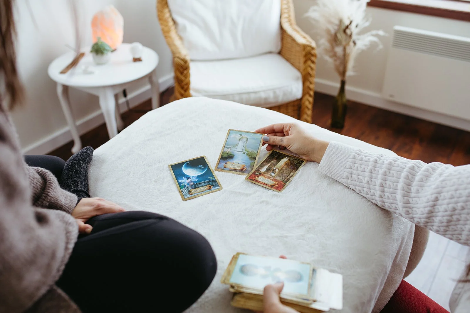 Stephanie Kamille's hand on a massage table with 3 oracle cards displayed and a chair in the back