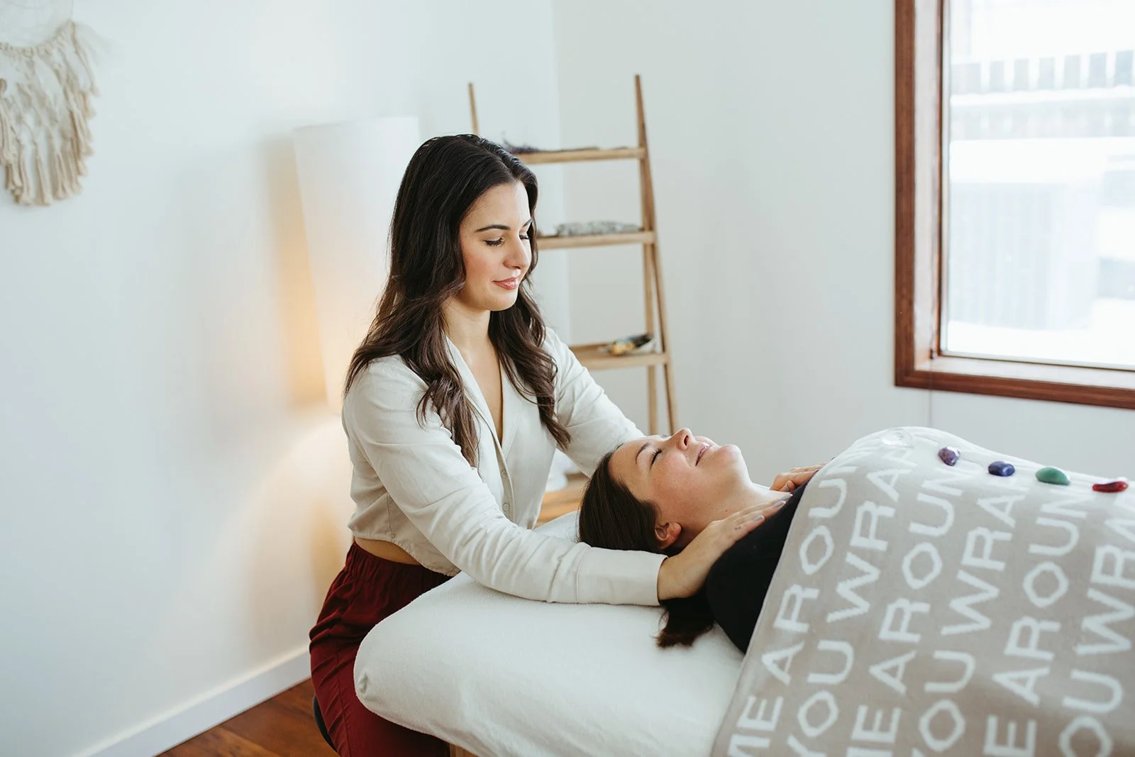 Stephanie Kamille giving Reiki to a woman on a massage table with a shelf in the back