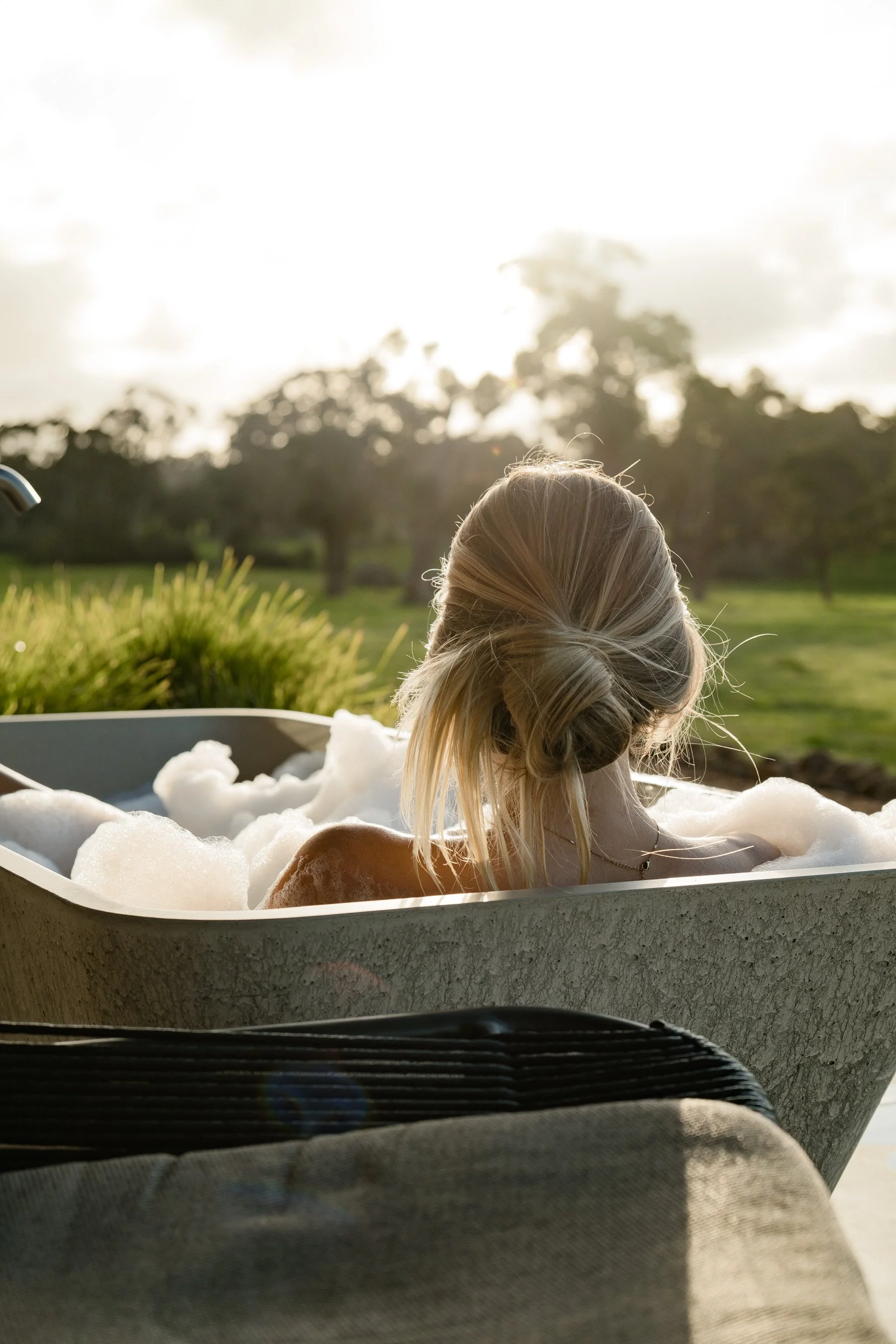 Image of gir in outdoor concrete bath relaxing over looking farm land