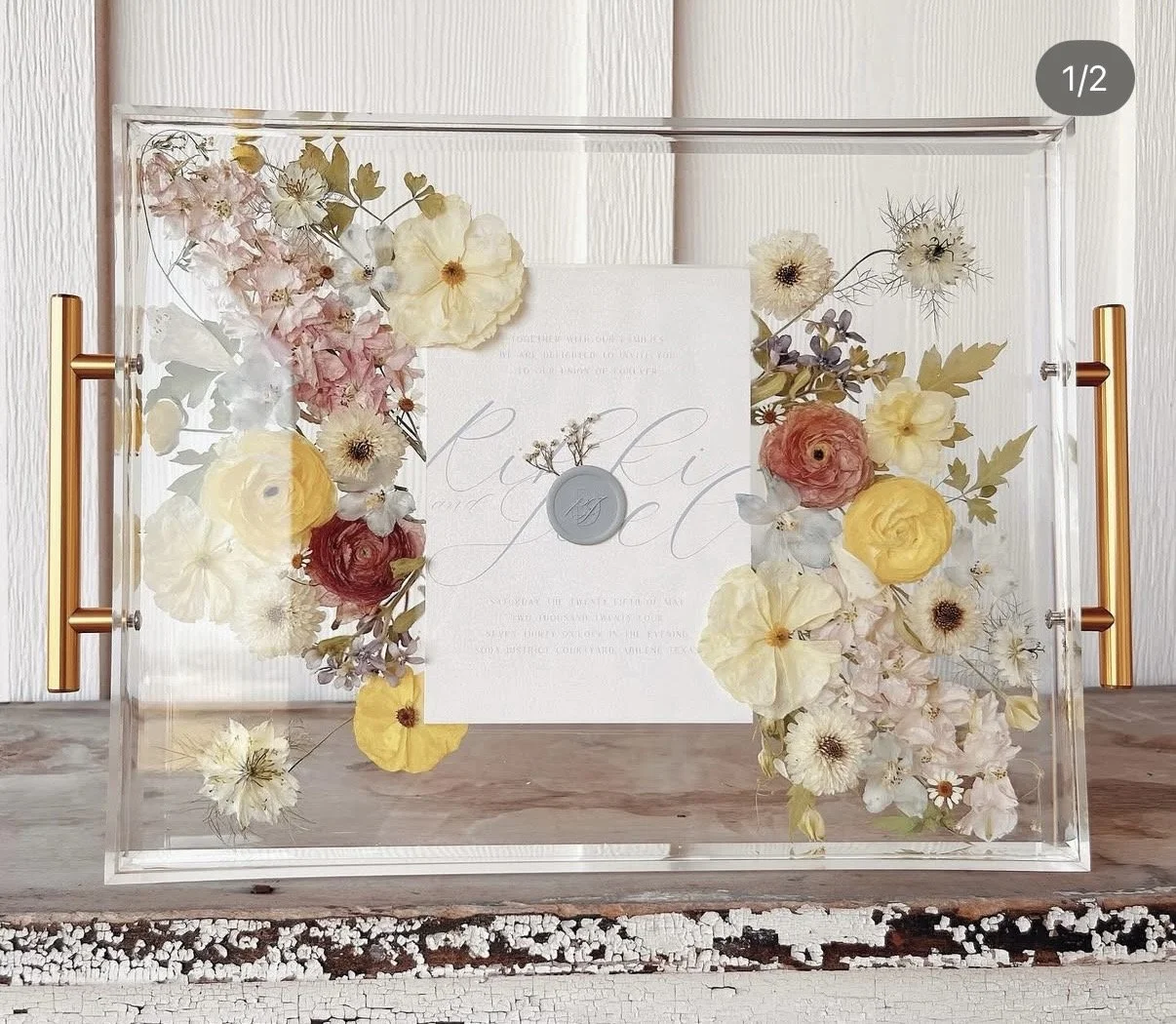 A transparent box with a bouquet of pastel-colored dried flowers inside, placed on a rustic wooden surface.