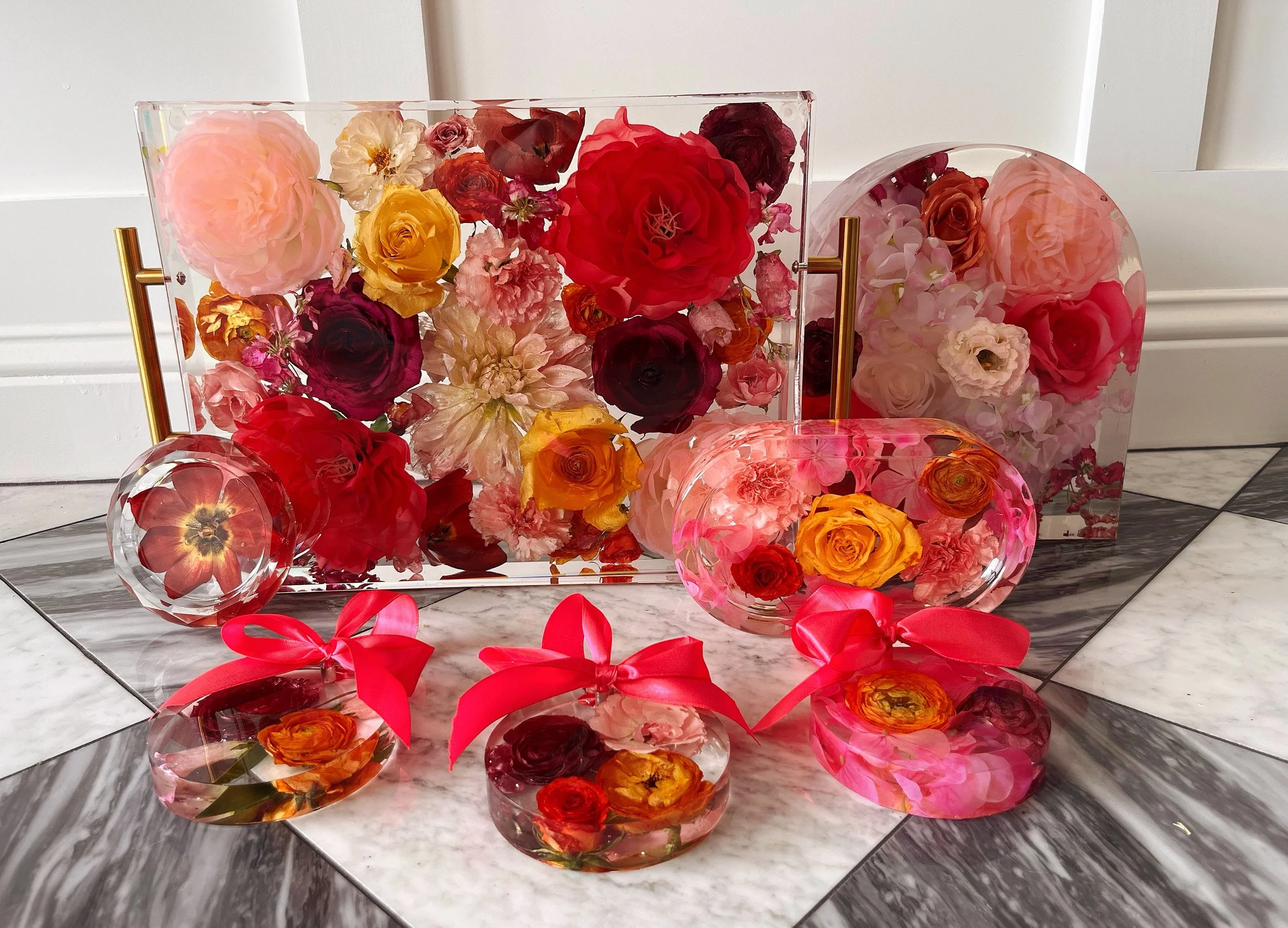 Decorative glass containers filled with colorful flowers, with red ribbons and bows, placed on a marble tiled floor.