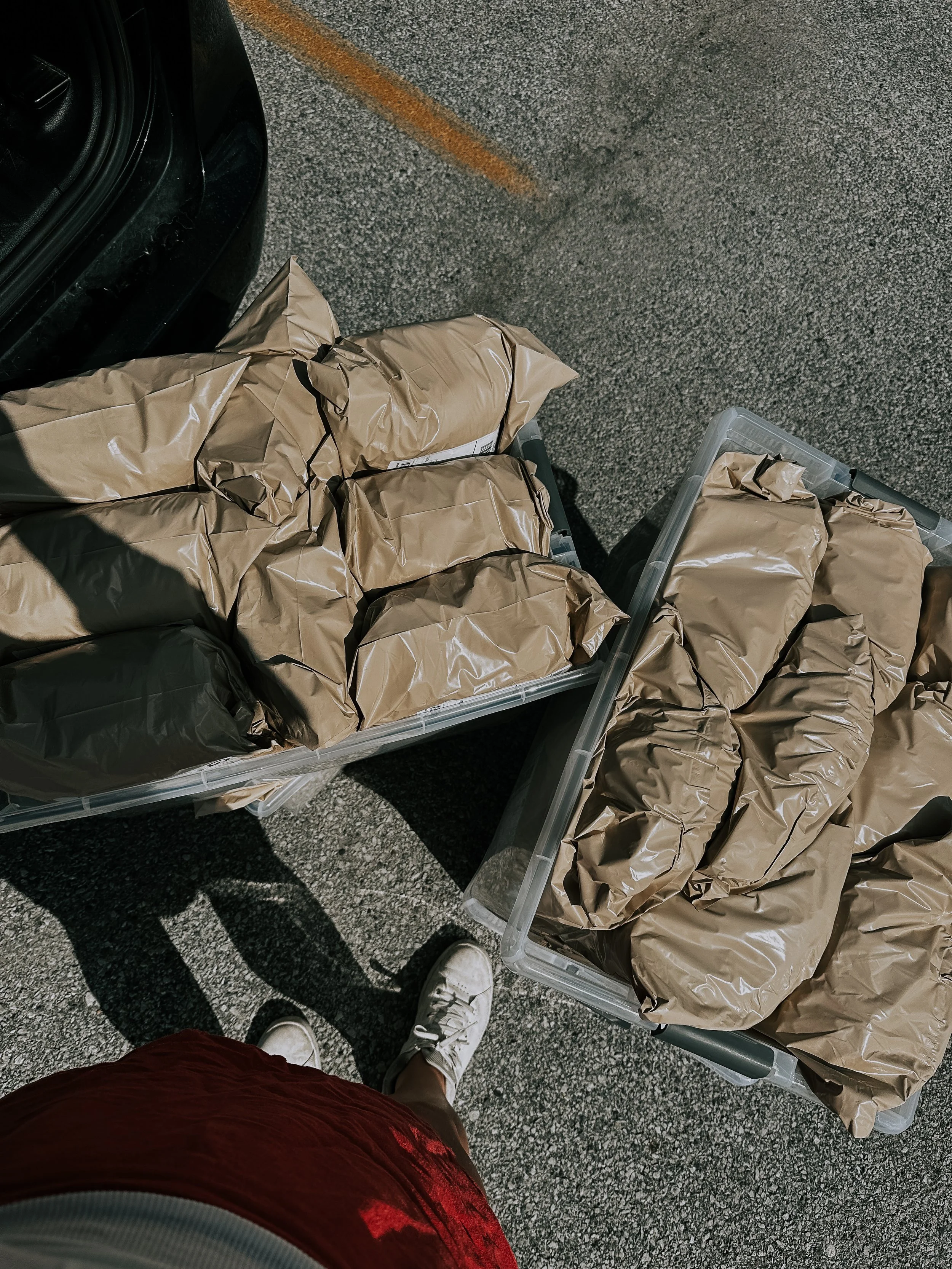 Two plastic bins filled with wrapped packages covered in brown paper, seen from above on a parking lot asphalt ground.