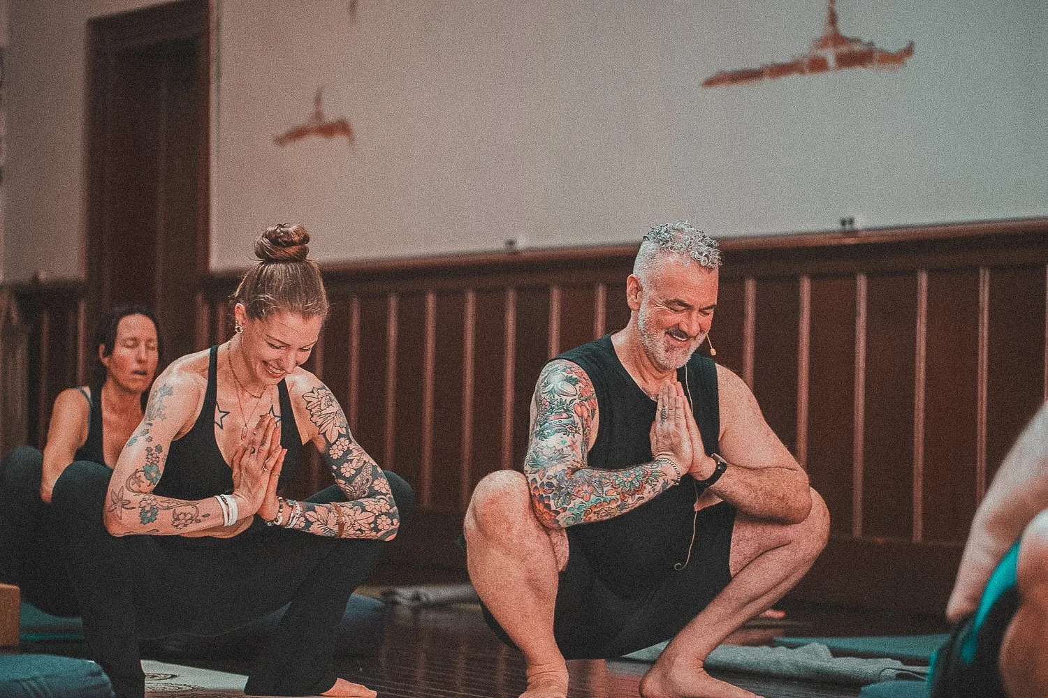 Group of people participating in a yoga or exercise class in a spacious room with wooden floors and large windows.