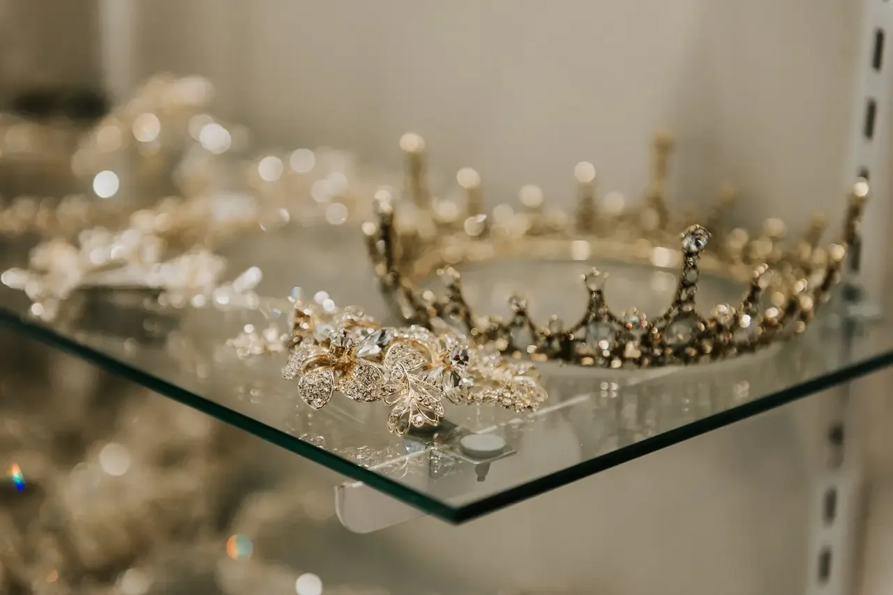 A display of jewelry including a gold tiara and a butterfly-shaped brooch with rhinestones on a glass shelf.