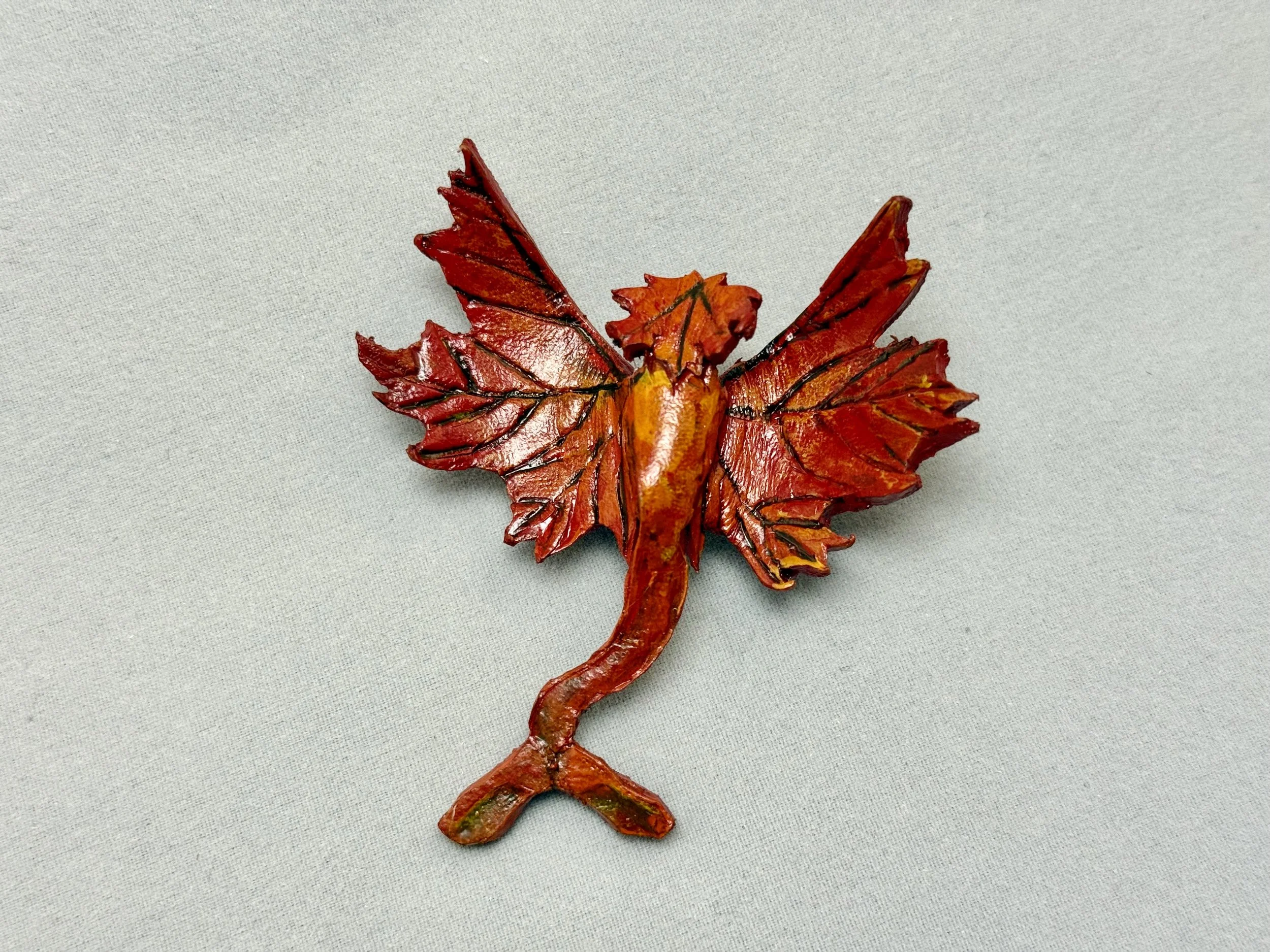 A small red leather dragon in the design of a autumn maple leaf by artist Bailey Maier