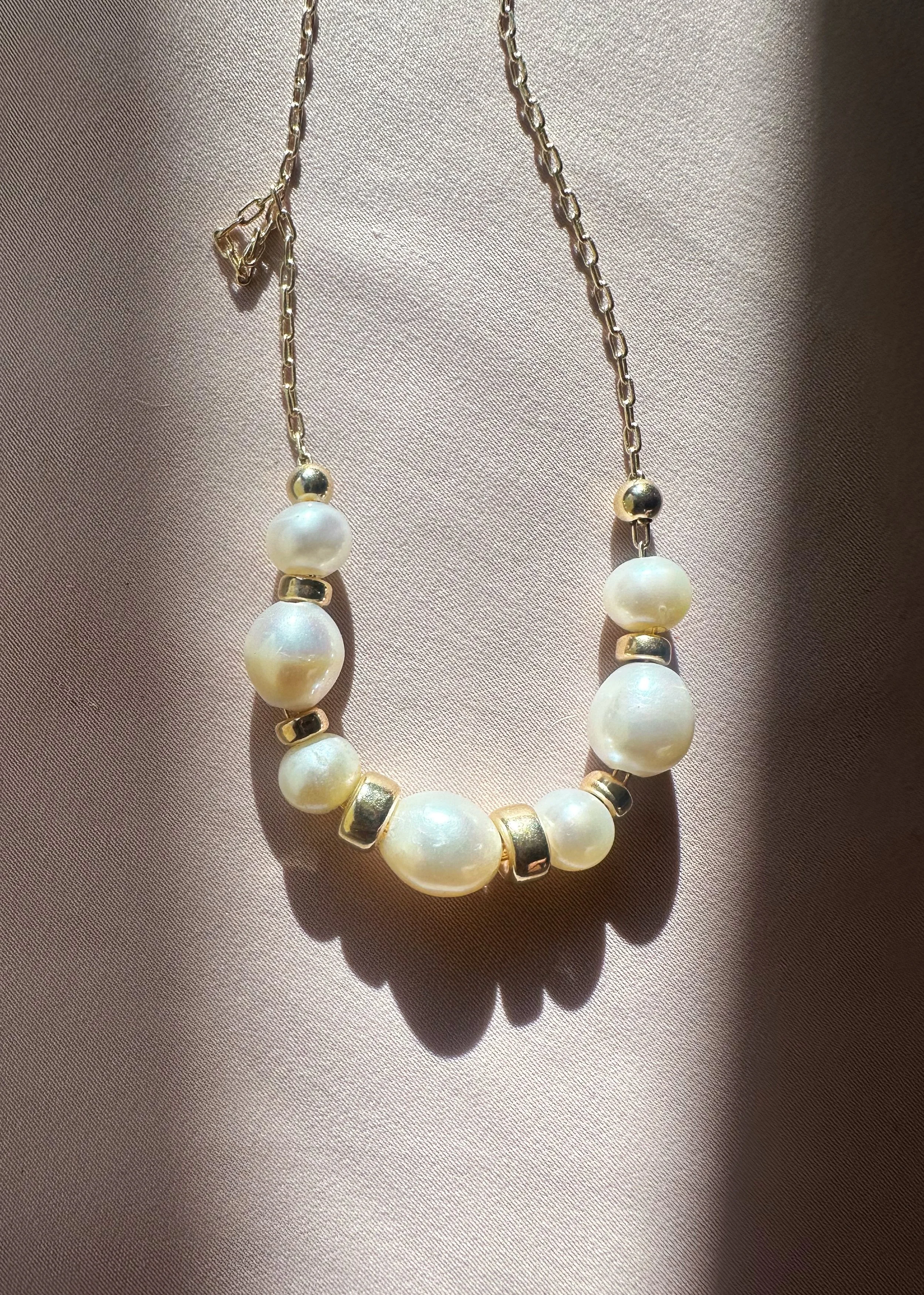 Close-up of The Vesper Necklace — floating baroque freshwater pearls and gold-filled beads on dainty fine chain, product shot on blush fabric