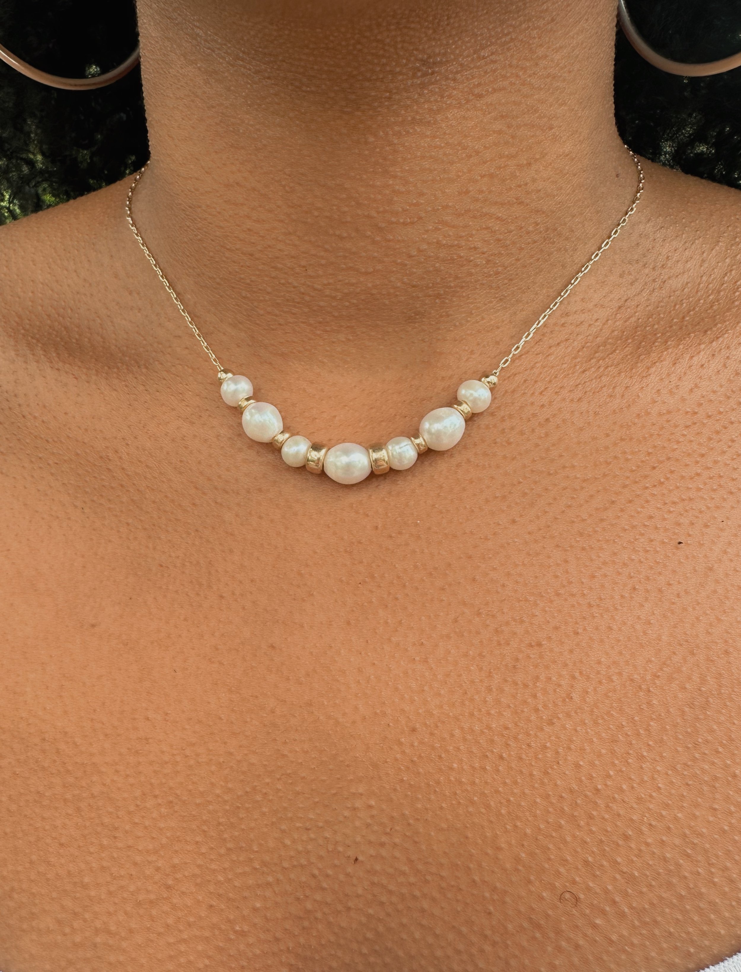 The Vesper Necklace on neck close-up — floating baroque pearl and gold-filled bead necklace on fine paperclip chain, model with dark hair