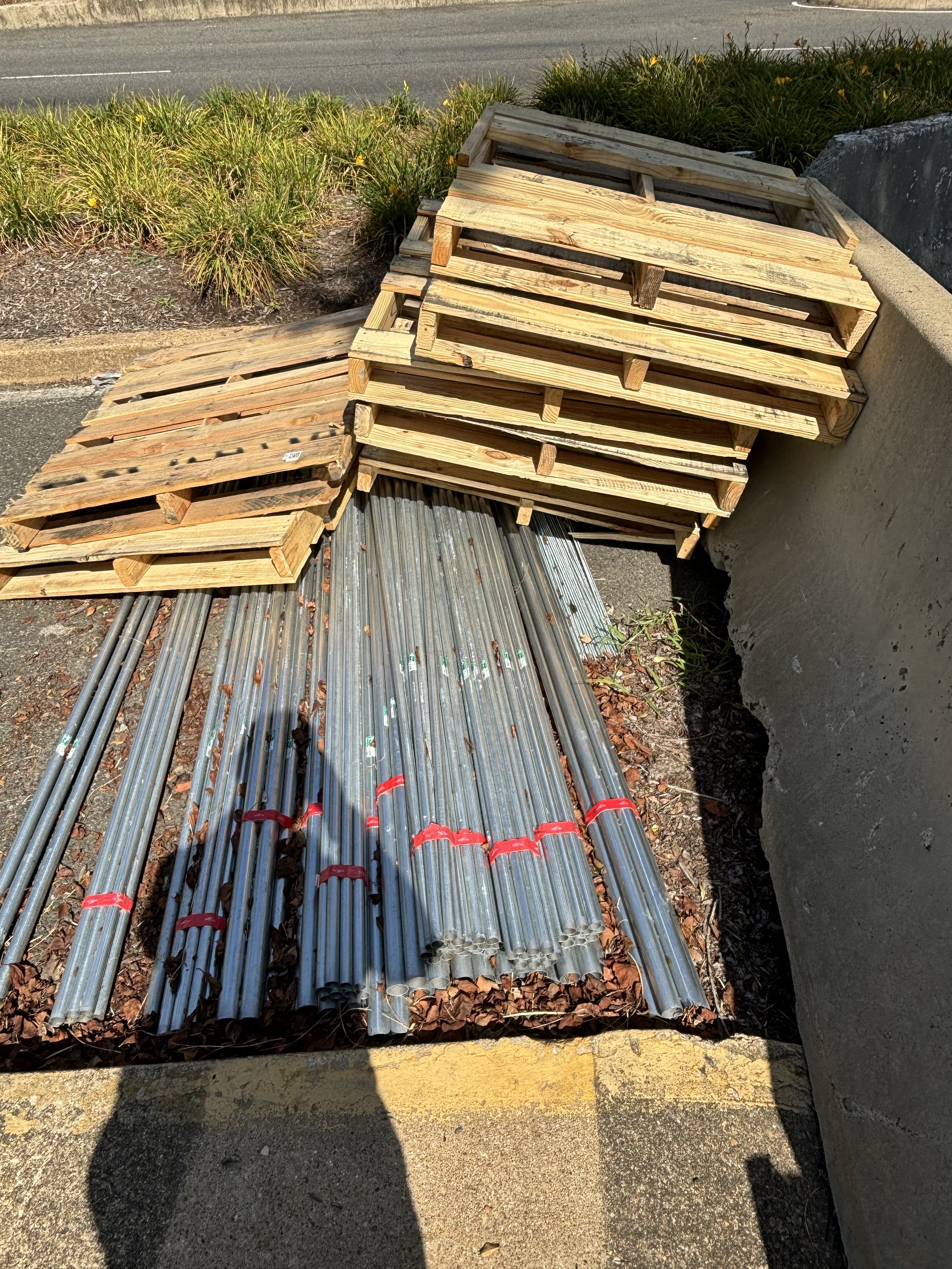 MANY DIFFERENT PIPES AND PALETTES WHICH HAVE BEEN LEFT NEAR TO THE ENTRANCE OF A CAR PARK