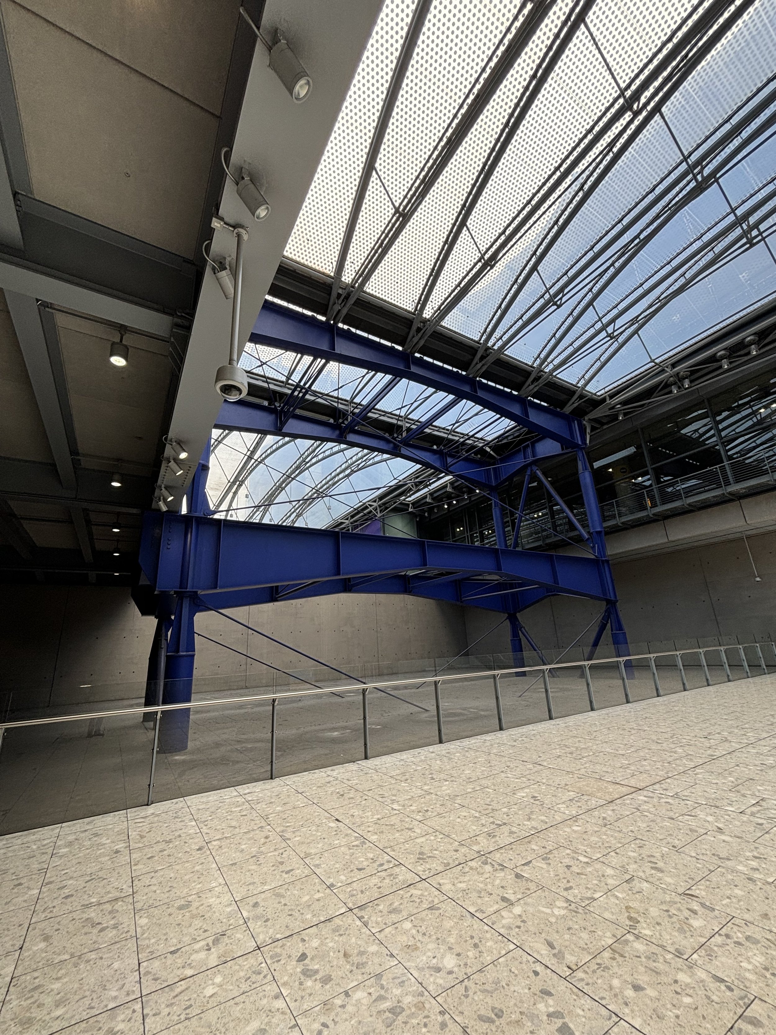 INSIDE THE TERMINAL - THERE ARE HUGE BLUE SUPPORTING STRUCTURES (BLUE). IT WOULD SEEM FITTING THE CONCRETE USED TO BUILD TERMINAL 5 WAS FROM AQUAMATED HUMANS. HOWEVER, THERE SEEMS TO BE AN ISSUE WITH THE HUMAN DNA INSIDE THE LIQUID AND IT'S CAUSING A
