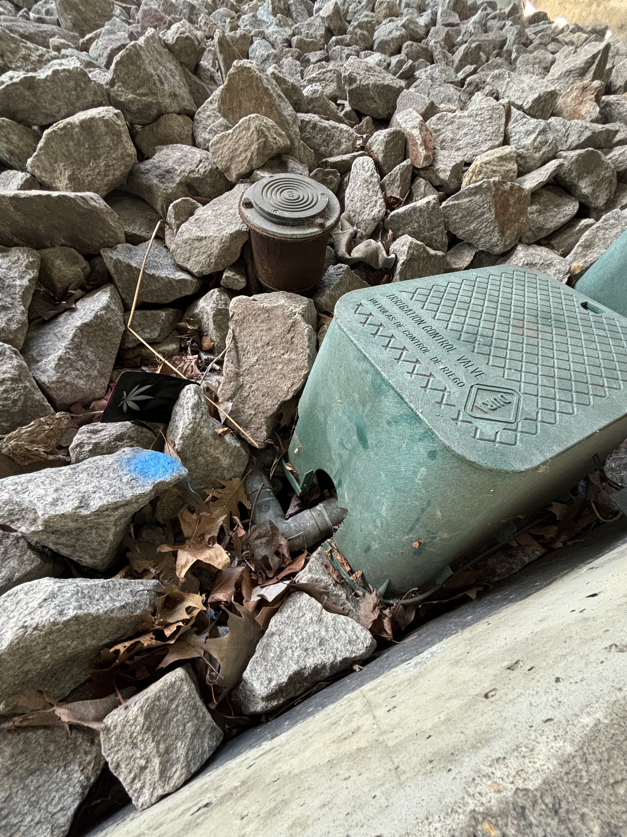 IN THE ROCK AREA, THERE ARE PIPES WHICH ARE HIDDEN UNDER A PLASTIC COVERING CALLED A 'IRRIGATION CONTROL VALVE'. IT IS A CONTINUATION OF A PIPE SYSTEM AND VERY CLOSE TO THE AREA OF THE FIRE HYDRANTS WITH WATER