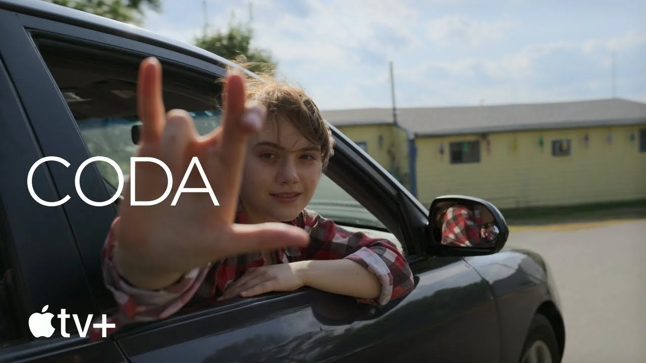 Poster for CODA. A white girl with light brown hair is leaning through a car window looking back, signing 'I love you' in ASL.