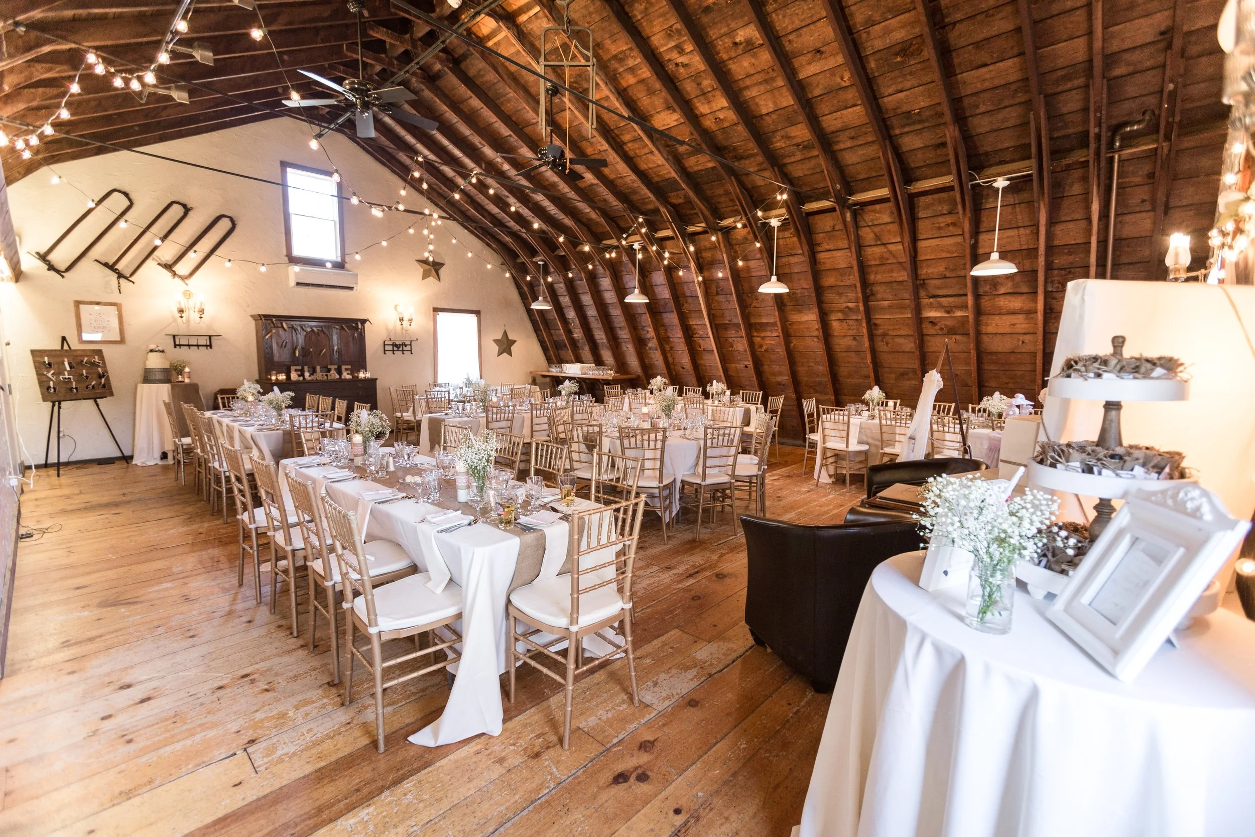 A rustic event room with wooden chairs arranged in rows, wooden vaulted ceiling, and natural lighting, decorated with stars, American flag, and antique skis on the wall.
