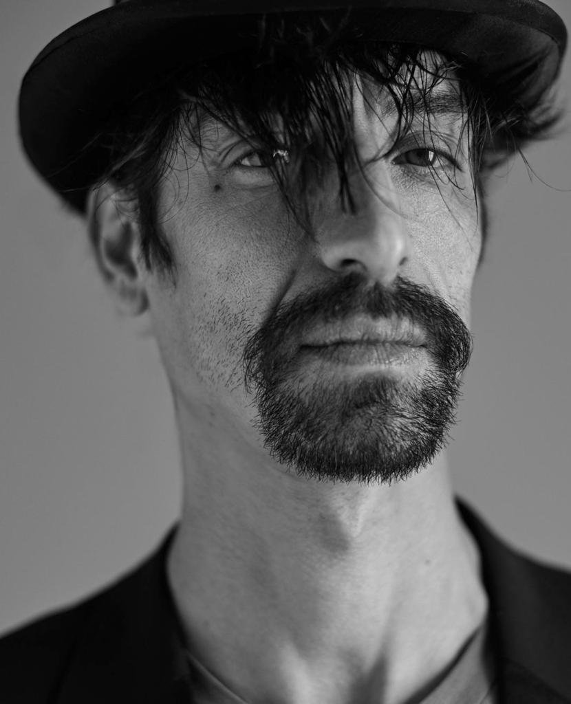 Black-and-white portrait of Paolo with a beard and messy hair, looking at the camera.