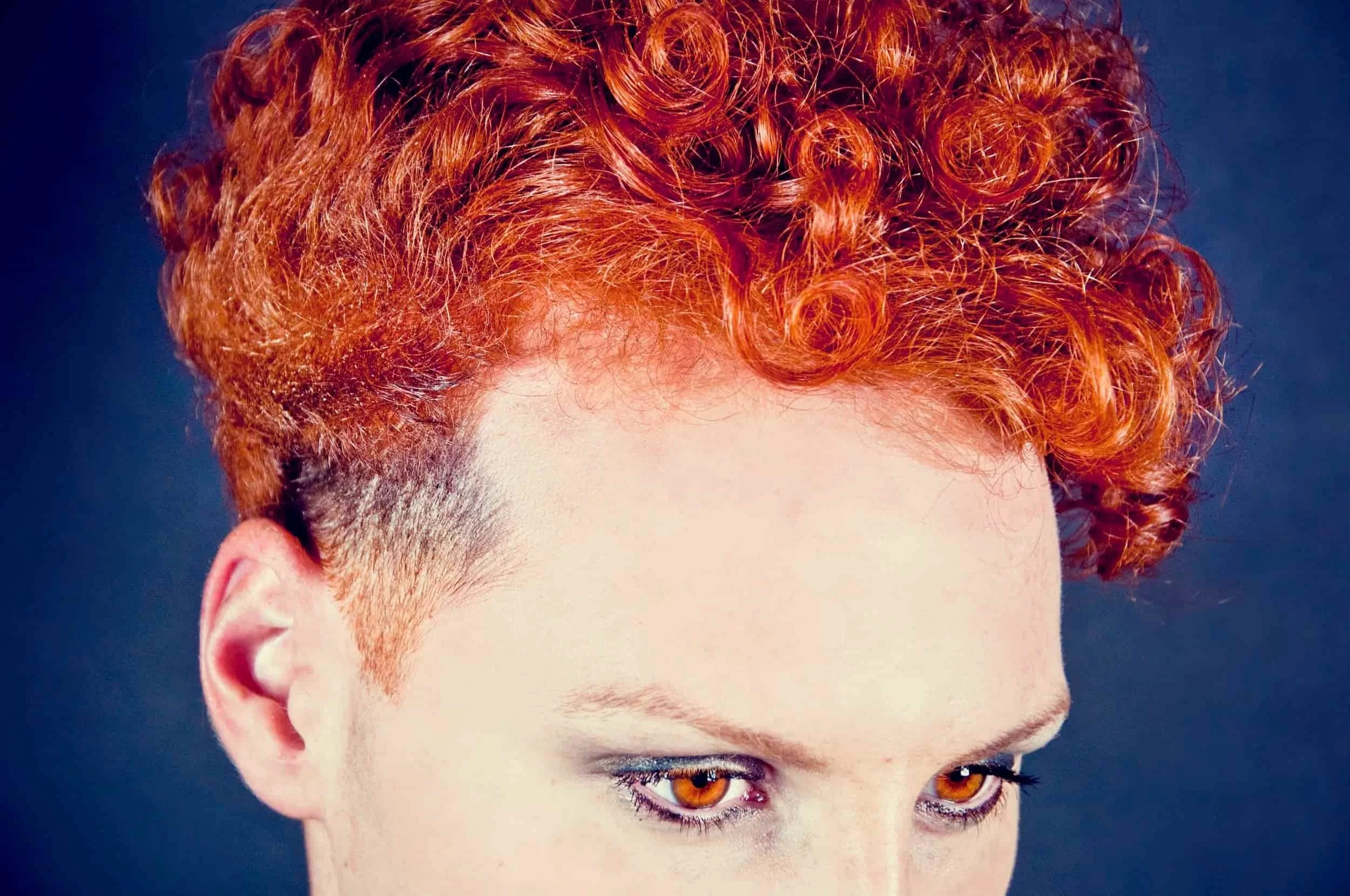Short undercut hairstyle with bright red curls styled voluminously on top.