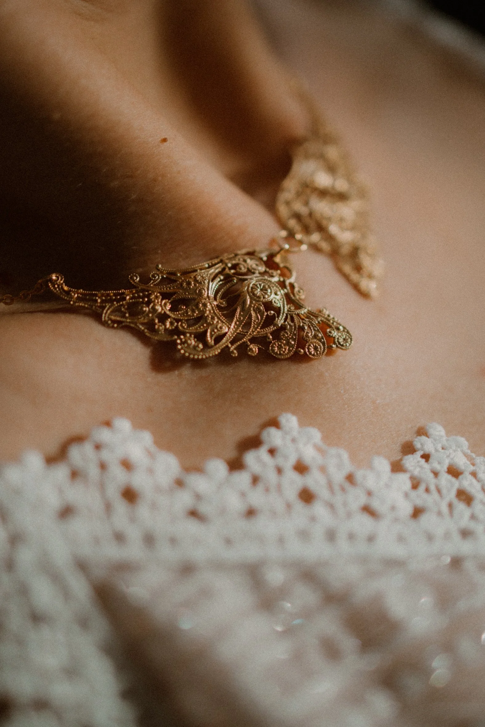 Gros plan d'une femme portant un collier en or complexe et délicat, avec des petites fleurs blanches en forme de perles ou de tissu séparée au premier plan.